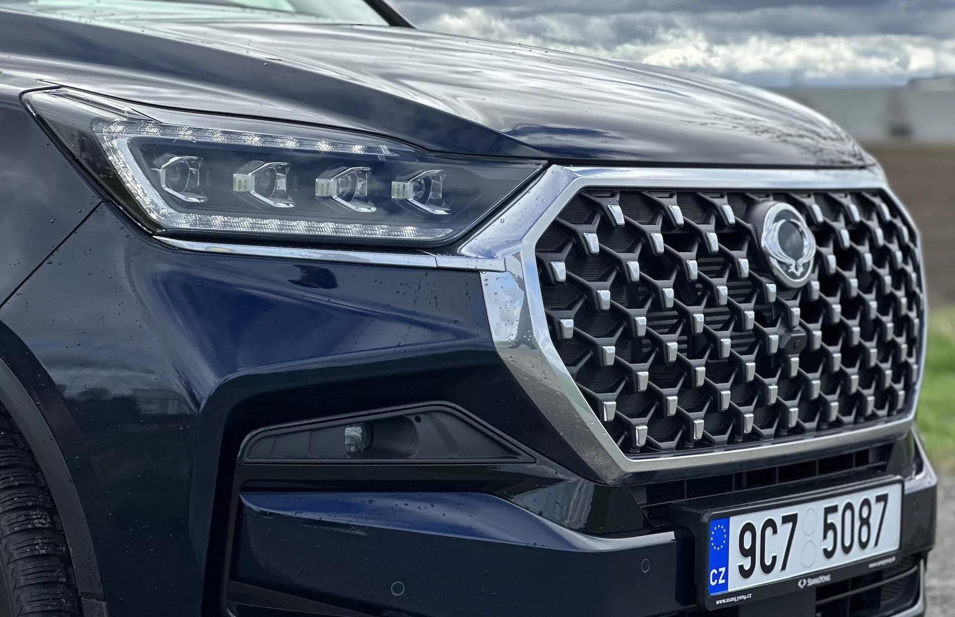 Vue angulaire avant du SsangYong Rexton 2021, se focalisant sur la grille, le pare-chocs avant et la conception des phares à LED, mettant en avant des fonctionnalités de sécurité avancées et de la technologie moderne avec une peinture métallique.