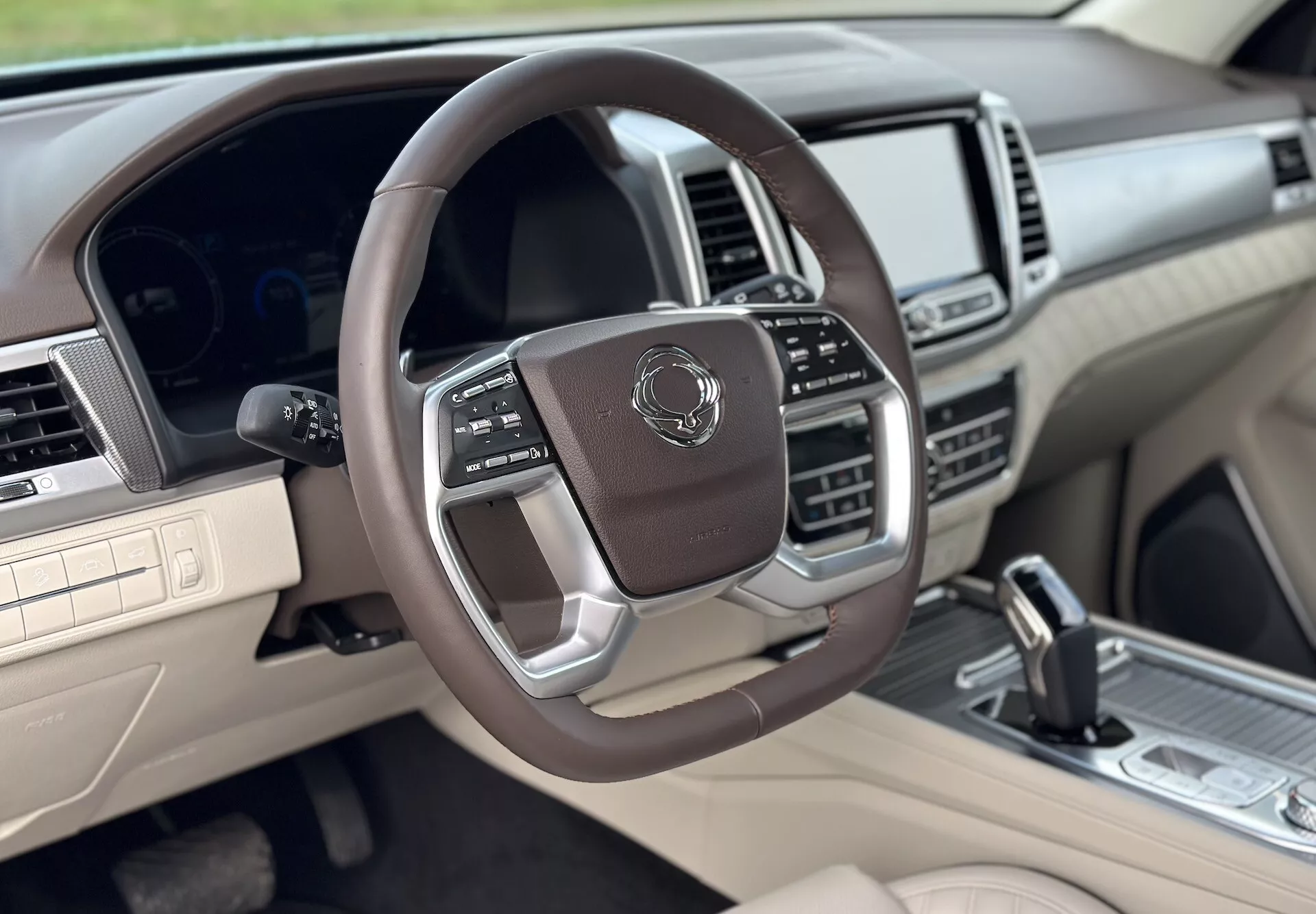 Vue de l'intérieur luxueux du SsangYong Rexton 2021 du côté passager avant, avec volant multifonctionnel enveloppé de cuir, accents métalliques, cluster d'instruments numériques, système d'infodivertissement avancé, et schéma de couleurs deux tons beige et foncé.