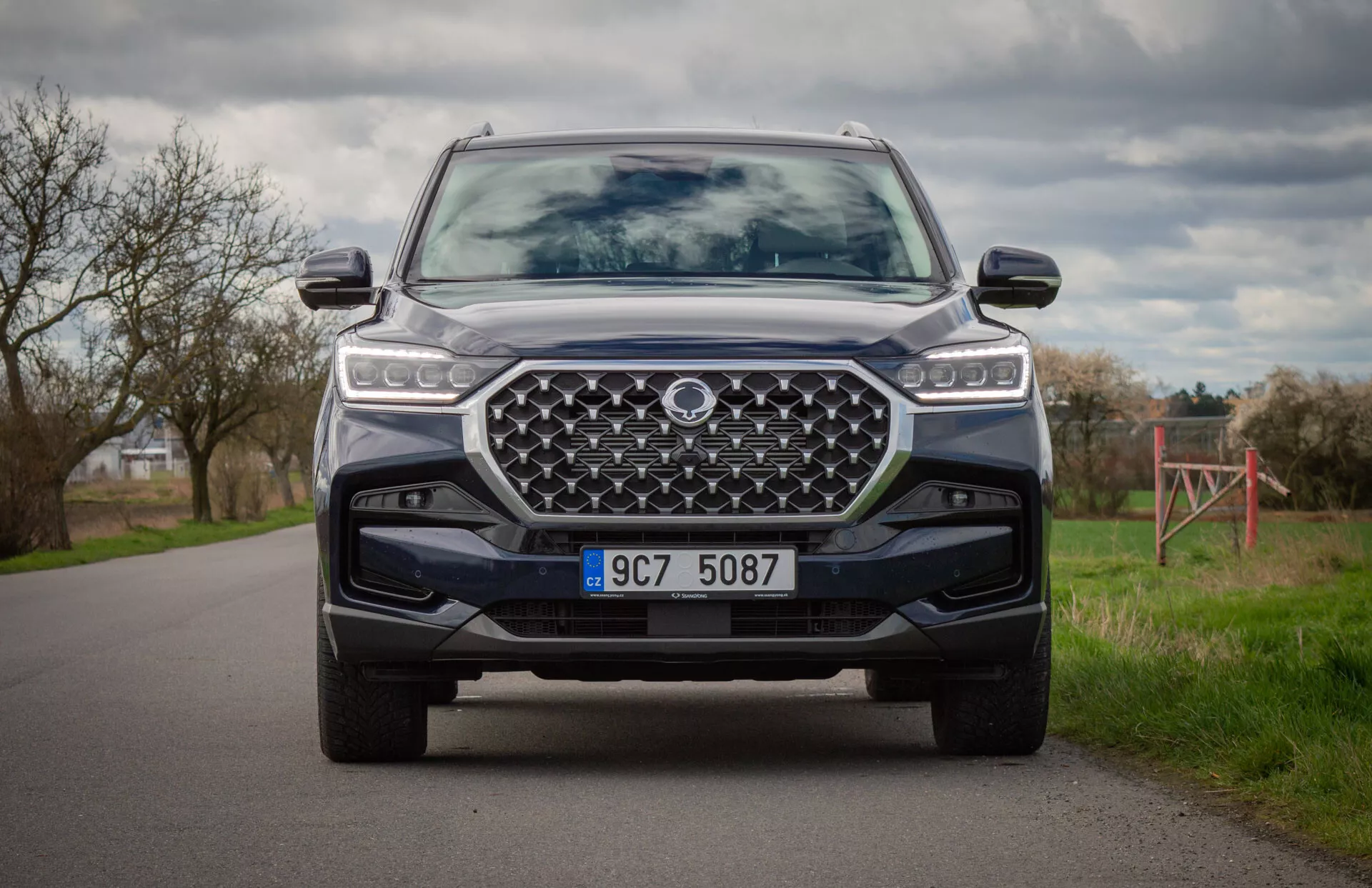 SUV moderne SsangYong Rexton 2021 en couleur, capturé depuis une position à genoux montrant l'avant du véhicule, phares LED, grande calandre dessinée, pare-chocs avant avec plaque de protection et systèmes avancés d'assistance au conducteur