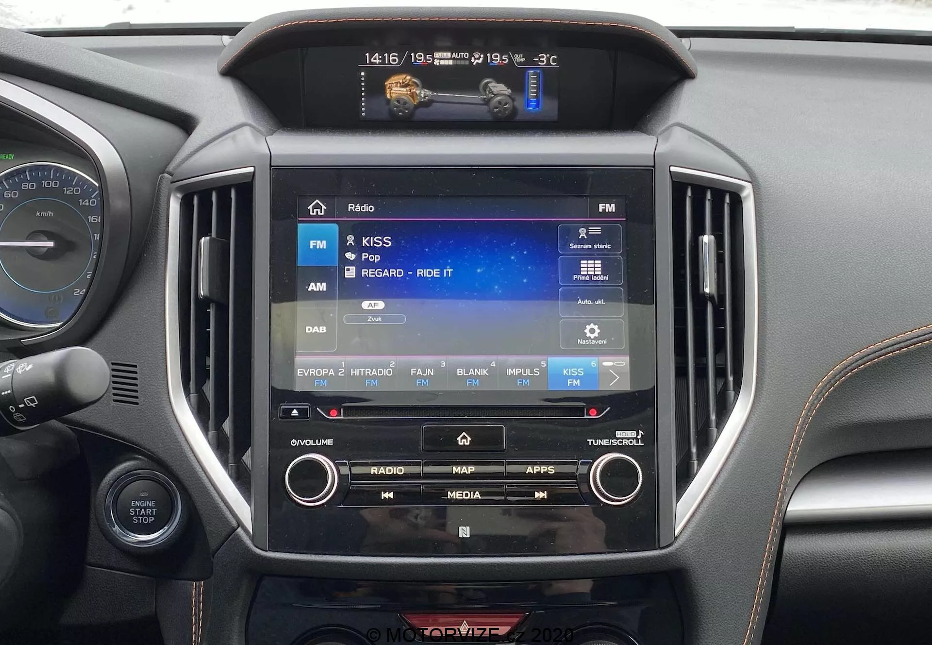 Vue en gros plan de l'intérieur de la Subaru XV 2018 (Subaru-XV-1-6i-Trend-Lineartronic) se concentrant sur le système d'infodivertissement central. L'écran tactile, d'environ 8 à 10 pouces, affiche une interface radio avec FM sélectionnée. Les éléments environnants comprennent des boutons physiques et des boutons de commande manuelle, un petit écran au-dessus indiquant -3°C, 14:16 et 19/05, ainsi que des bouches d'aération symétriques. Le matériau autour du système a une finition métallique noire ou gris foncé, typique des intérieurs de voitures modernes. Une partie du tableau de bord et du volant sont également visibles.