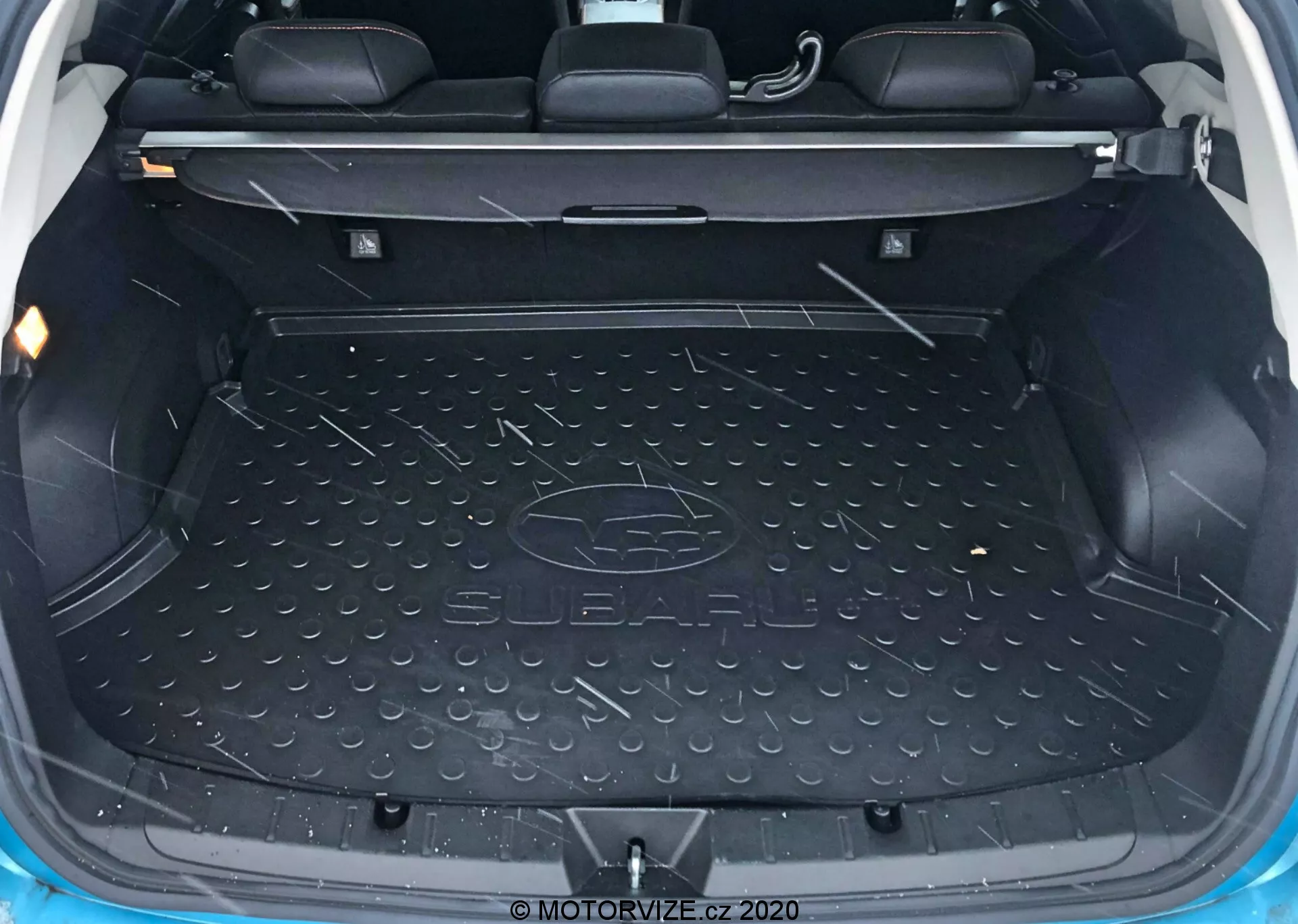 Vue intérieure du coffre du Subaru XV 2018 montrant une zone de chargement spacieuse et vide, doublée d'un tapis résistant à l'eau et durable avec le logo Subaru, des compartiments moulés de chaque côté pour le rangement de petits objets, les dossiers des sièges arrière visibles avec des appuie-têtes indiquant qu'il s'agit probablement d'un véhicule 5 places, un mécanisme de sièges arrière rabattables divisés, des points d'ancrage et des crochets pour sécuriser la cargaison et un éclairage intérieur pour la visibilité.
