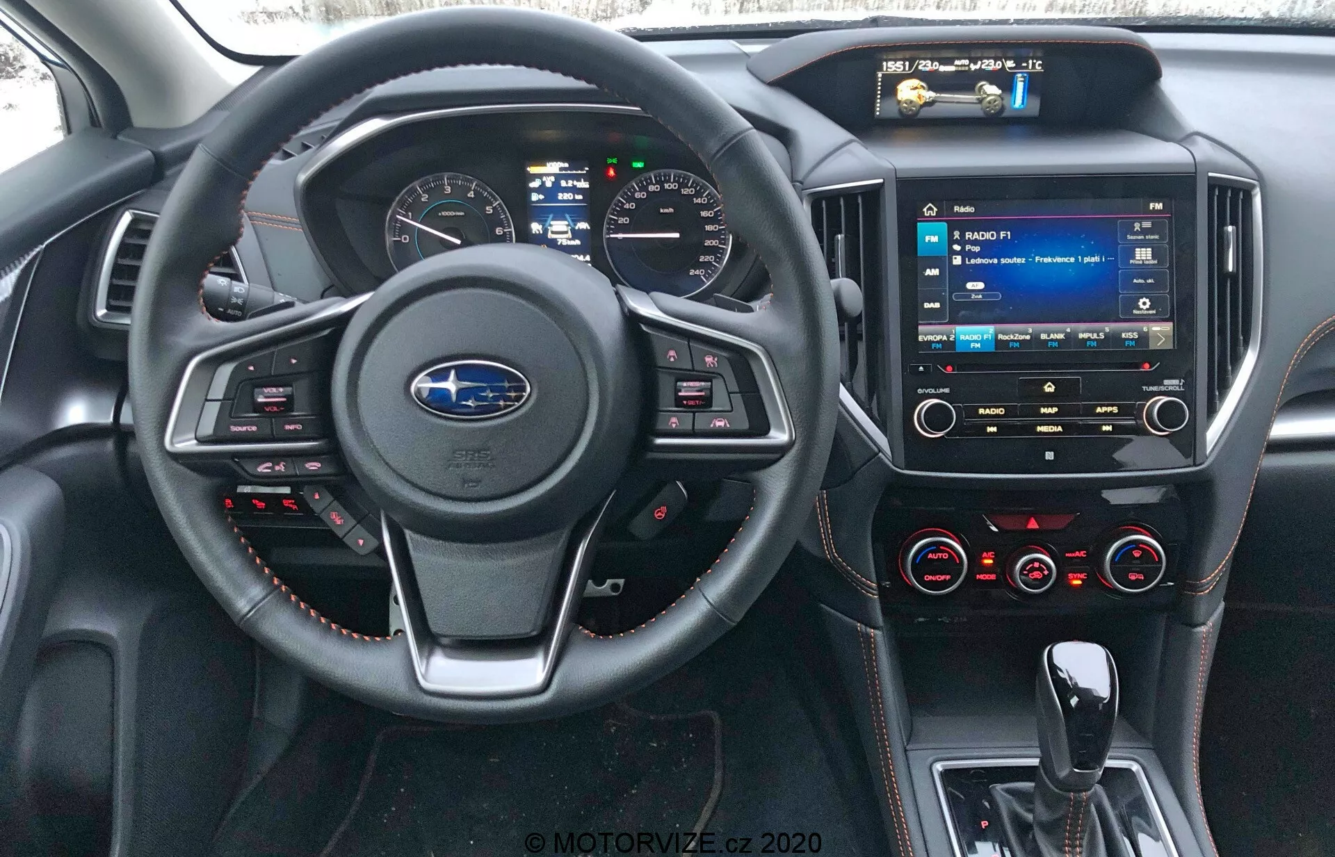 Vue intérieure de la Subaru XV 2018 depuis la place du conducteur, montrant le logo Subaru sur le volant avec boutons de commande, détails de couture rouge, tableau de bord numérique, système multimédia à écran tactile sur la console centrale, boutons de contrôle de la climatisation, ports USB, entrée audio de 3,5 mm et matériaux de type cuir avec coutures rouges sur le tableau de bord et les panneaux de porte.