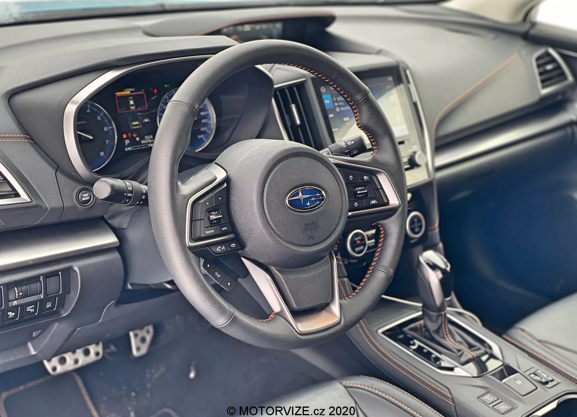 Vue détaillée de l'intérieur de la Subaru XV 2018 (Subaru-XV-1-6i-Trend-Lineartronic) focalisée sur l'espace conducteur, présentant un tableau de bord fonctionnel avec un volant de marque Subaru comprenant des commandes intégrées pour l'audio et les appels mains libres, un tableau de bord visible avec compteur de vitesse, compte-tours et écran numérique, un écran d'infodivertissement central intégré dans le tableau de bord, ainsi que des boutons de commande de climatisation. La console centrale dispose d'un levier de vitesses automatique en position de stationnement et d'autres boutons pour les modes de conduite, associés à des matériaux et des éléments de design modernes et élégants.