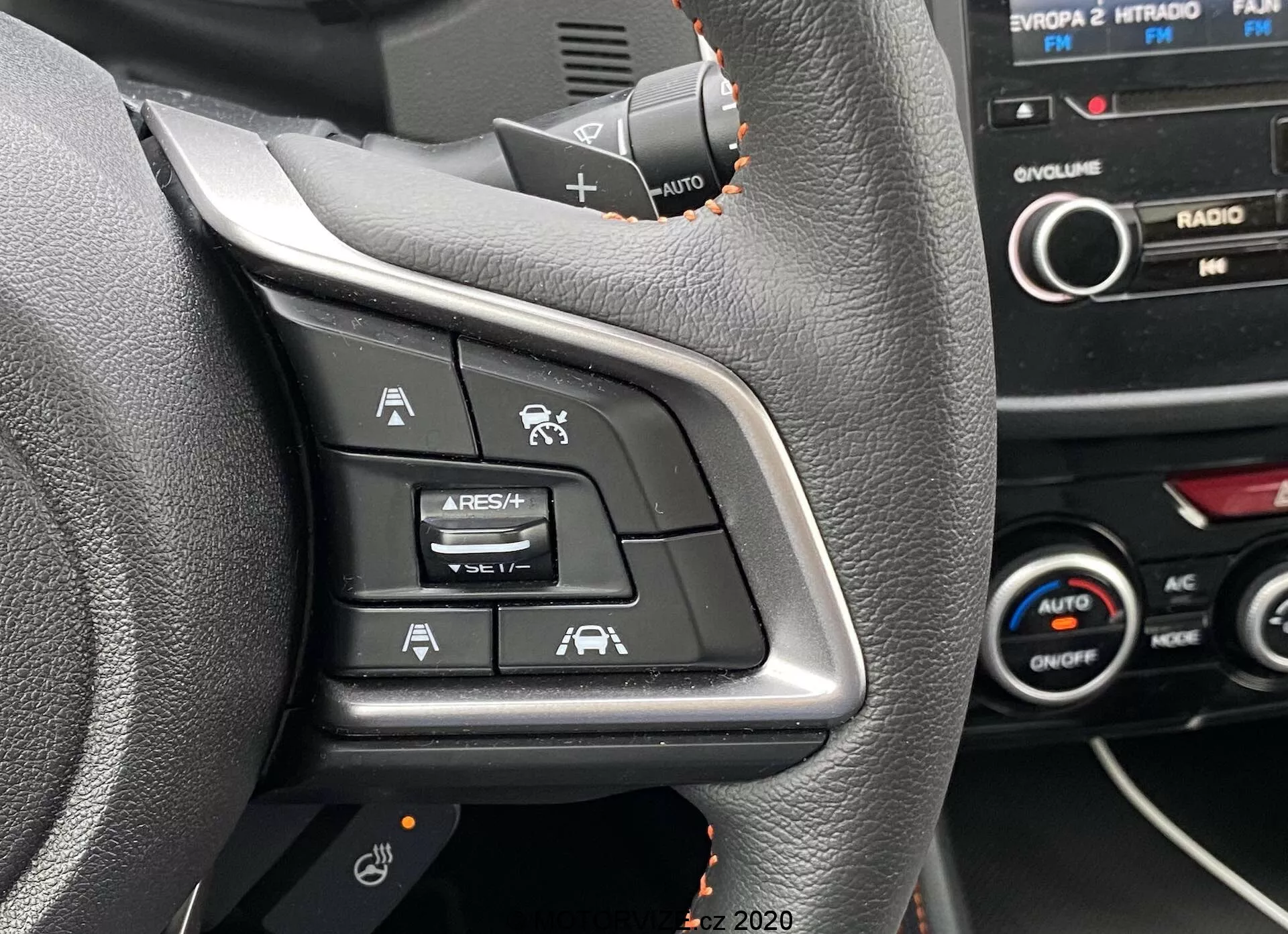 Vue rapprochée des commandes sur le côté gauche du volant d'une Subaru XV 2018, avec des boutons pour le régulateur de vitesse adaptatif, le limiteur de vitesse, la commande vocale et l'assistance au maintien de la voie. La prise de vue est faite depuis le siège du conducteur, mettant en évidence les symboles éclairés sur une surface en plastique noir, avec une partie du tableau de bord et de la console centrale visible en arrière-plan.