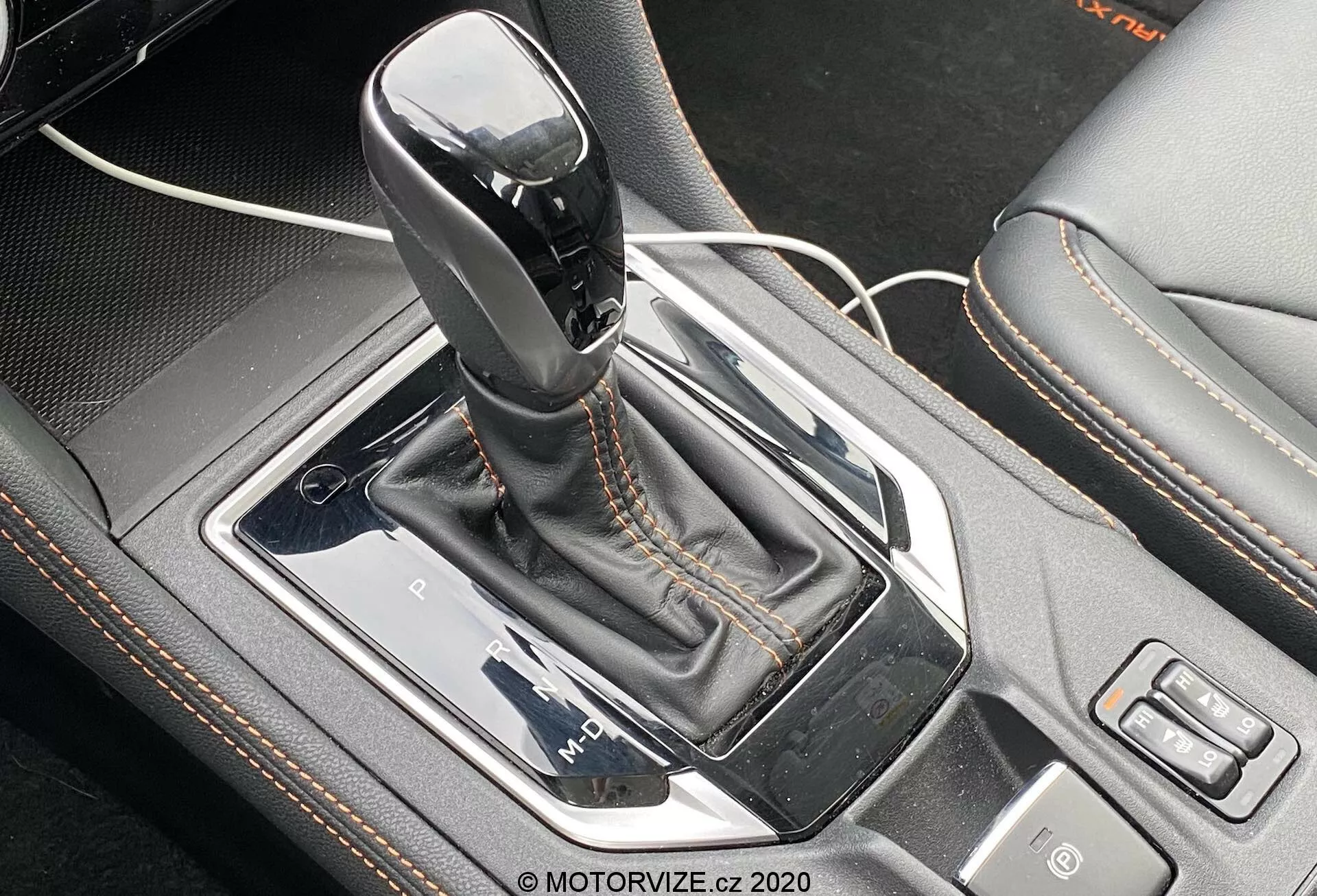 Vue de près de la levier de vitesses automatique Lineartronic du Subaru XV 2018 1.6i Trend. Le levier de vitesses, en position de stationnement, avec une partie supérieure noire brillante et un accent argenté, est positionné au centre de la console centrale de la voiture. Il est entouré d'un panneau argenté, encastré dans un cadre métallique noir brillant avec un soufflet en similicuir doté de coutures contrastées. À gauche, un câble USB indique un port à proximité, tandis qu'à droite, les boutons pour la sélection du mode de conduite et une autre fonction sont visibles. La perspective d'en haut et légèrement en avant met en valeur les détails de conception complexes et les fonctionnalités technologiques de la zone du levier de vitesses.