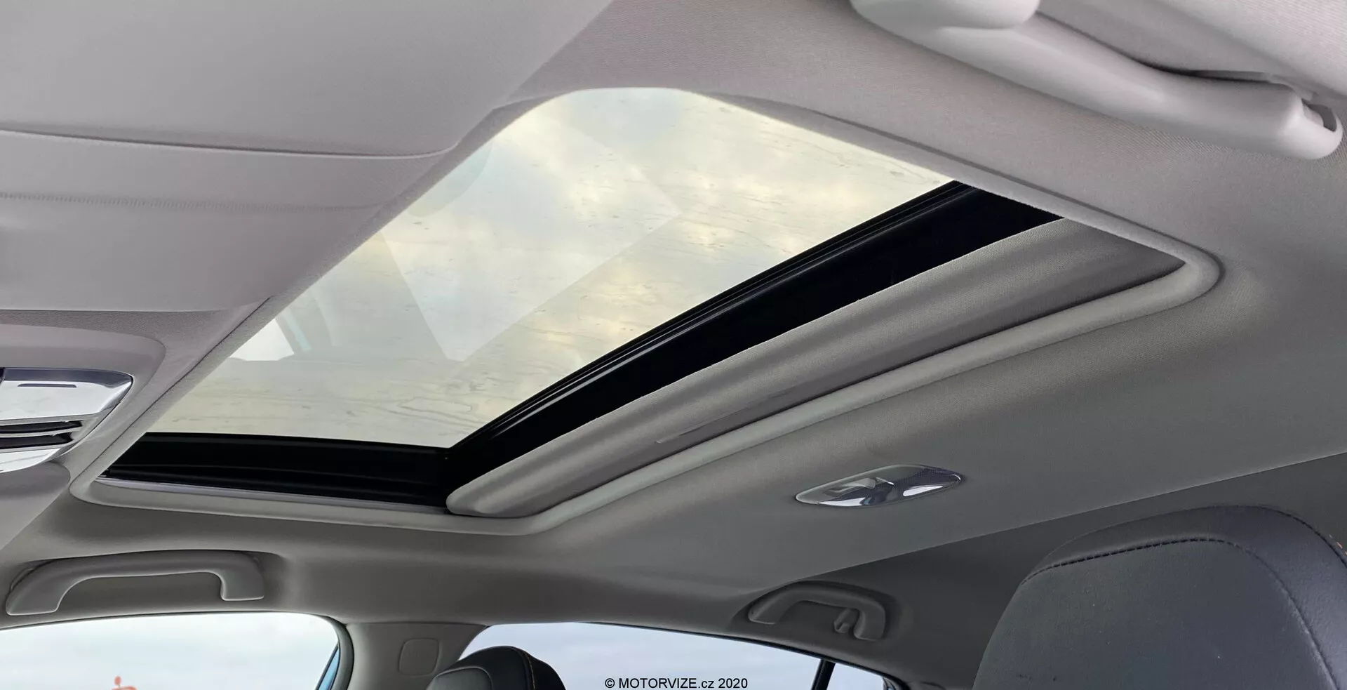 Vue intérieure de la Subaru XV 2018 1.6i Trend Lineartronic se concentrant sur le grand toit ouvrant panoramique. Le toit s'étend de l'avant à l'arrière de l'habitacle, partiellement ouvert avec un mécanisme coulissant. Le verre teinté offre une protection UV, améliorant le sentiment d'espace à l'intérieur. La garniture intérieure entourant le toit est de couleur claire, complétant l'esthétique moderne. Les lumières LED intégrées au plafond sont visibles, indiquant un éclairage efficace et durable.
