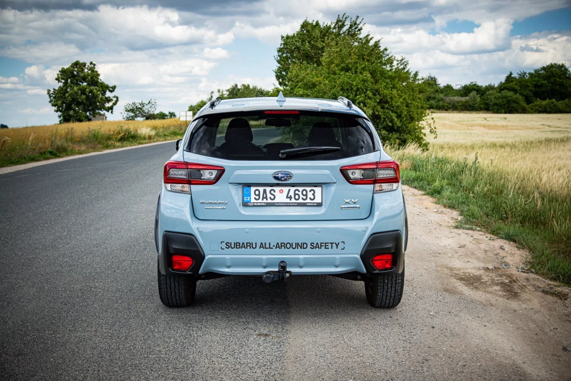 Vue arrière d'une Subaru XV 2021 sur une route rurale, montrant les feux arrières distinctifs de la voiture, le système d'échappement double et le hayon étiqueté sécurité sous un ciel partiellement nuageux