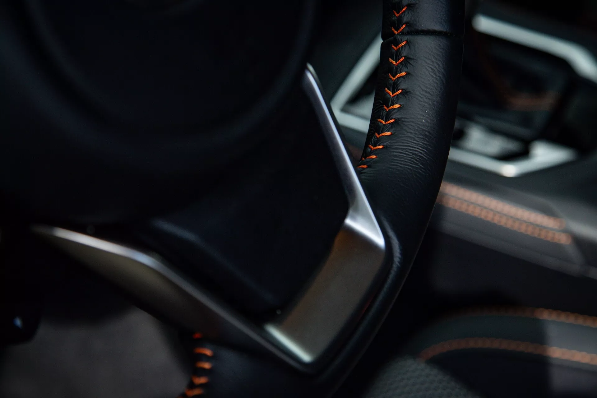 Vue détaillée de l'intérieur du Subaru XV 2021 se concentrant sur le côté conducteur avec une partie du volant en couleur noire et des coutures orange ou rouge, à côté d'un panneau de porte détaillé avec du cuir ou du simili cuir noir et des accents de garniture métallique