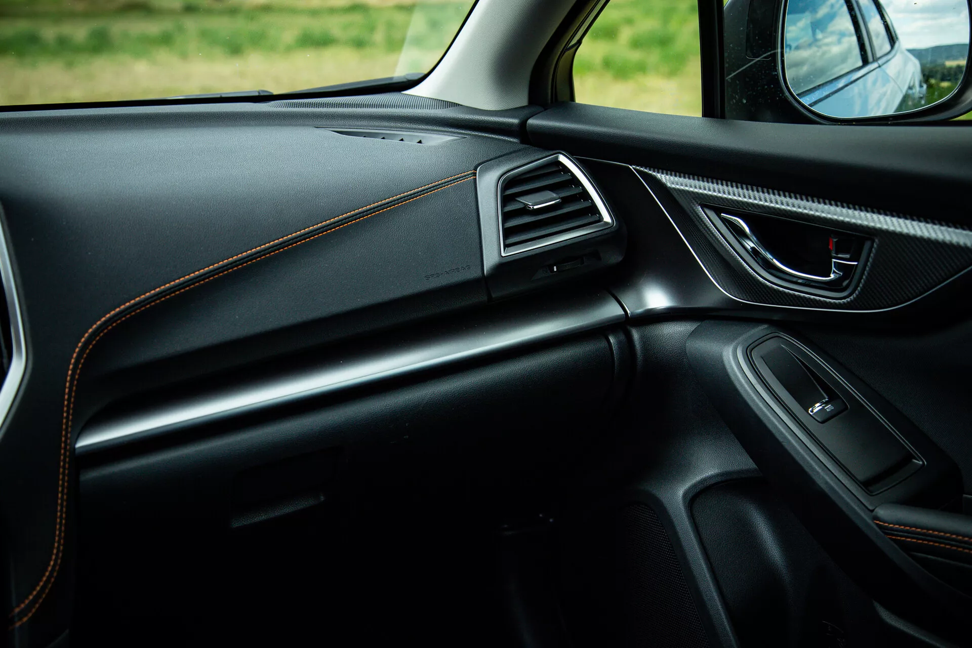 Vue intérieure de la Subaru XV 2021 se concentrant sur le côté passager montrant le design élégant du tableau de bord avec coutures contrastées, poignée de porte ergonomique avec commandes électriques, haut-parleur intégré, aérations accentuées de chrome et éclairage d'ambiance