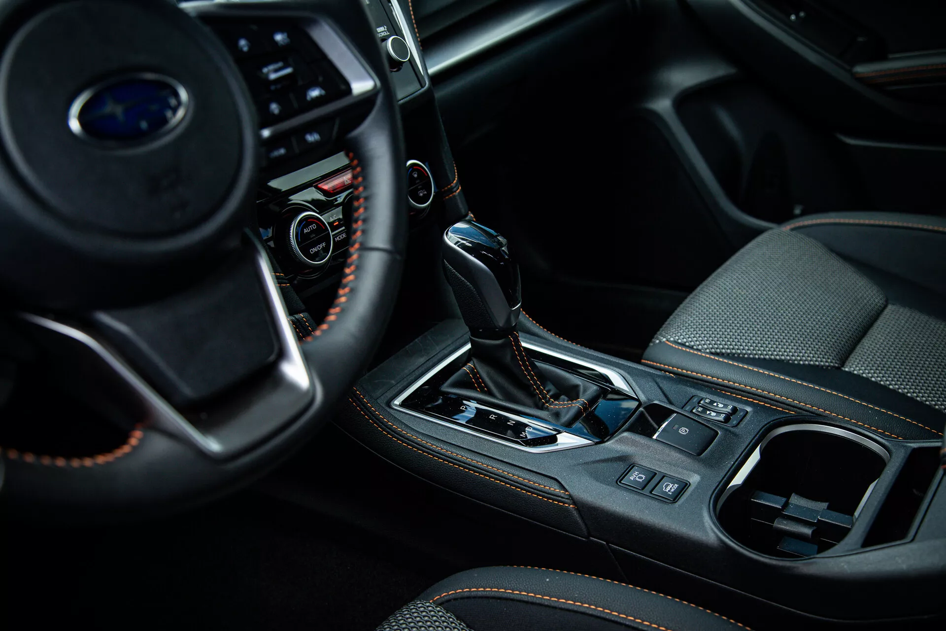 Vue rapprochée de l'intérieur d'une Subaru XV 2021 centrée sur la console centrale et la zone du levier de vitesse du côté passager, montrant des boutons multifonctions sur le volant, un sélecteur de transmission automatique avec soufflet en cuir et accents métalliques, et des fonctionnalités de design intérieur haut de gamme telles que le frein à main électronique et le système de contrôle du climat.