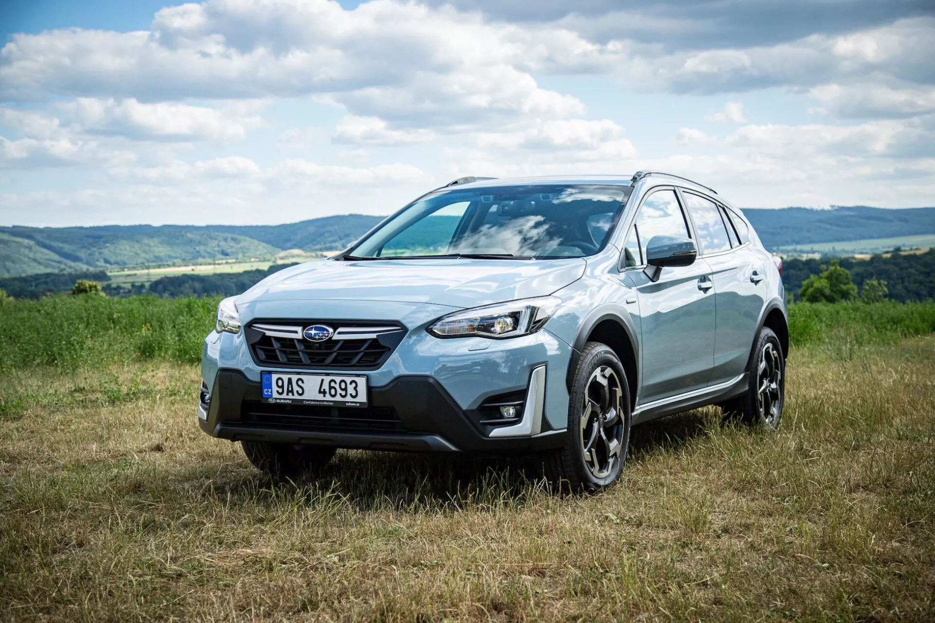 SUV crossover Subaru XV 2021 garé sur l'herbe avec un arrière-plan vallonné, mettant en évidence la façade avant, le profil latéral et le design de la roue