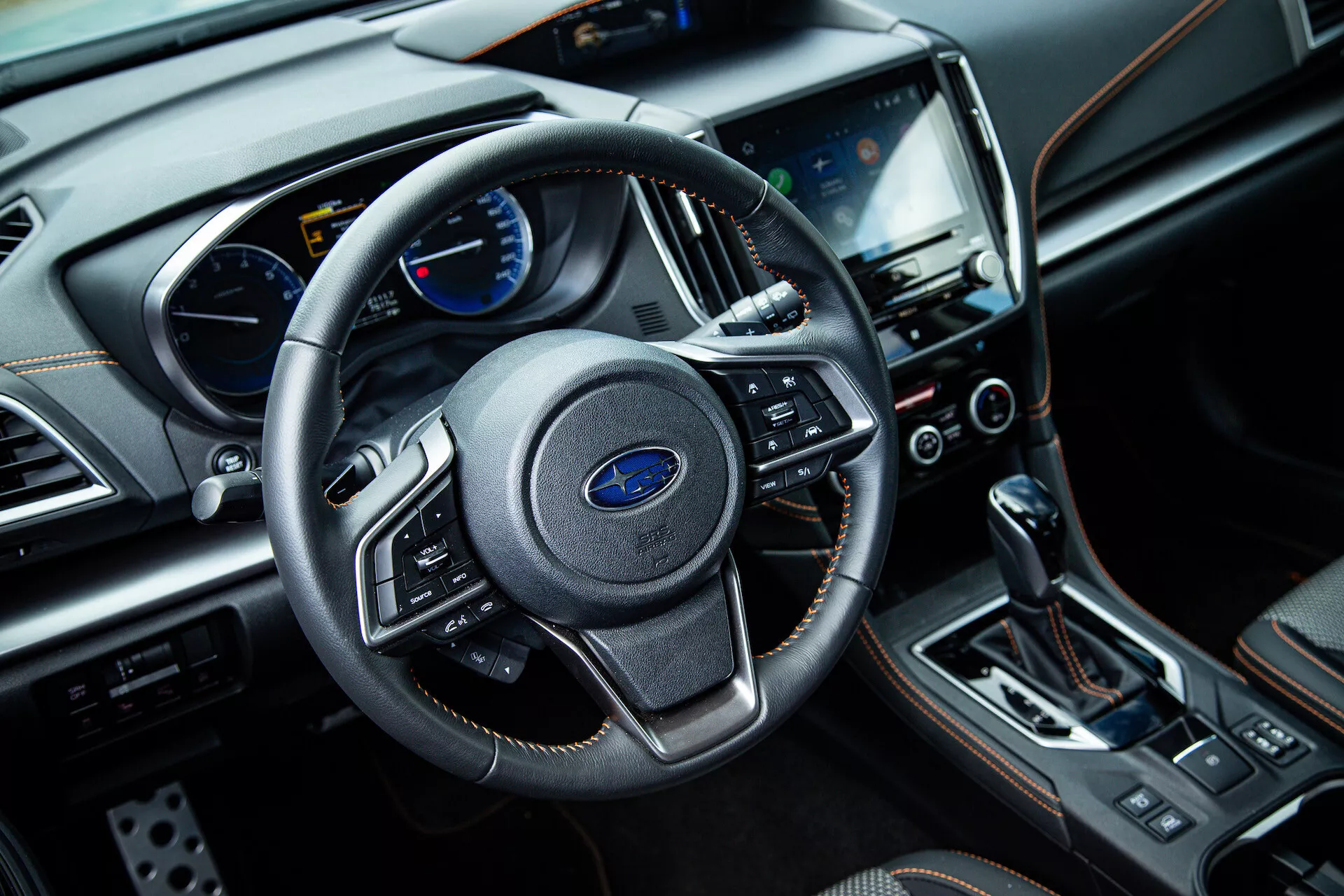 Vue intérieure du Subaru XV 2021 depuis le côté passager avant présentant un volant à trois branches avec commandes multifonctions, un tableau de bord avec affichages analogiques et numériques, un système d'infodivertissement central tactile, des boutons de contrôle climatique, un levier de changement de vitesse automatique, et des matériaux de finition de luxe, y compris le cuir et les accents chromés.