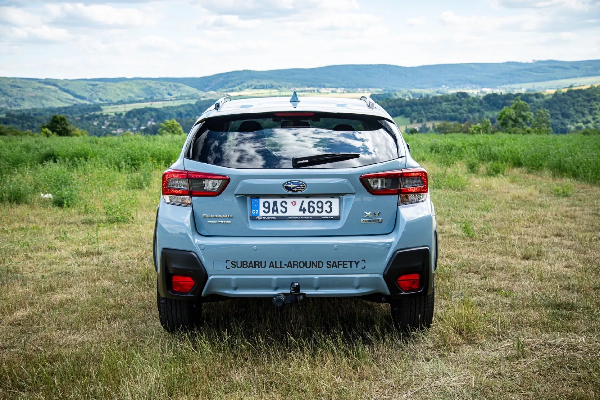 Vue arrière en angle du Subaru XV 2021 en extérieur dans un champ avec un arrière-plan vallonné, mettant en évidence les caractéristiques de sécurité et les éléments de design moderne SUV comme l'aileron arrière et les feux arrière audacieux