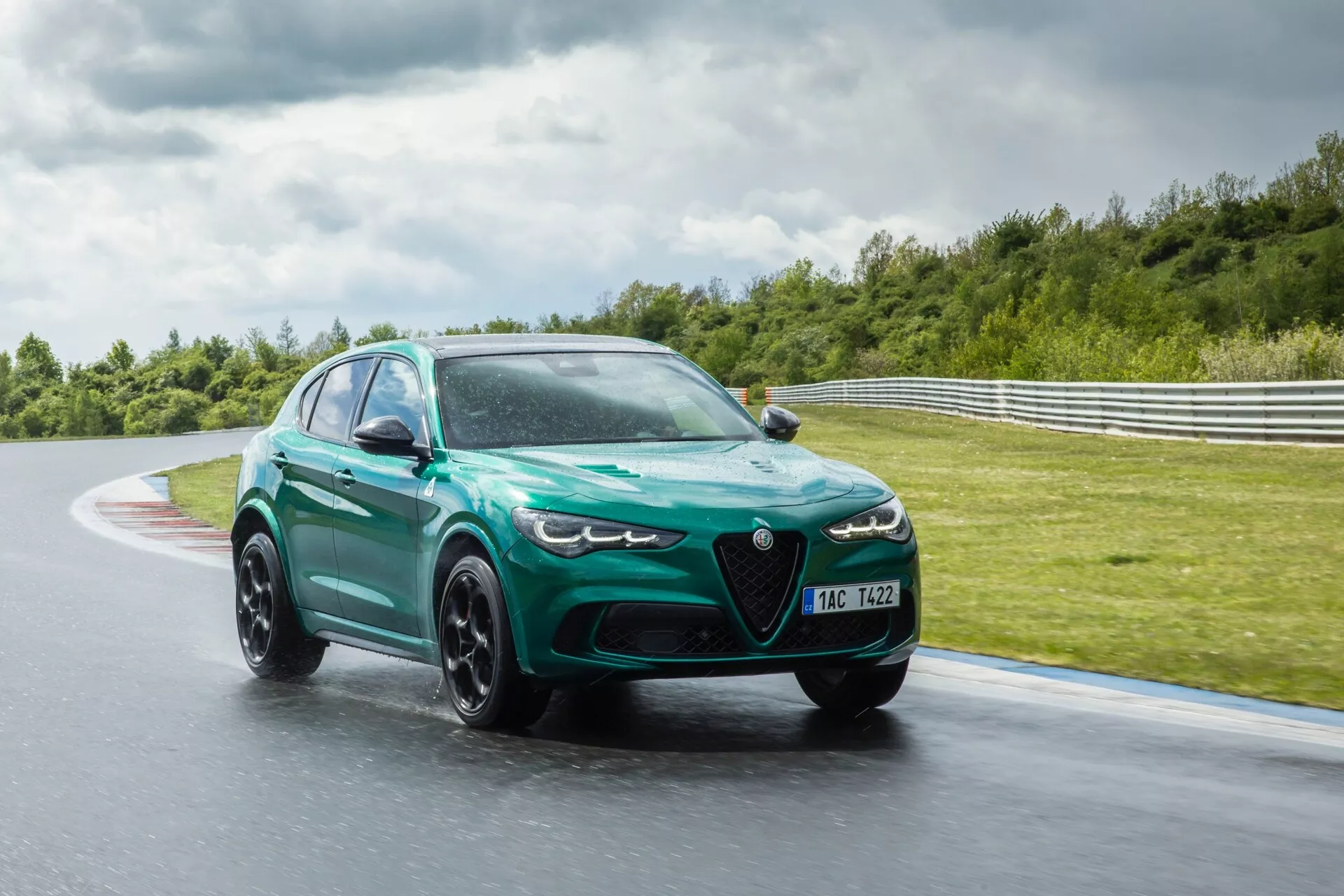 Alfa Romeo Giulia Quadrifoglio 2023 en mouvement sur une piste de course mouillée, présentant un design aérodynamique avec de grandes entrées d'air, des phares LED agressifs et une peinture verte métallique avec des roues noires mates à multiples branches.