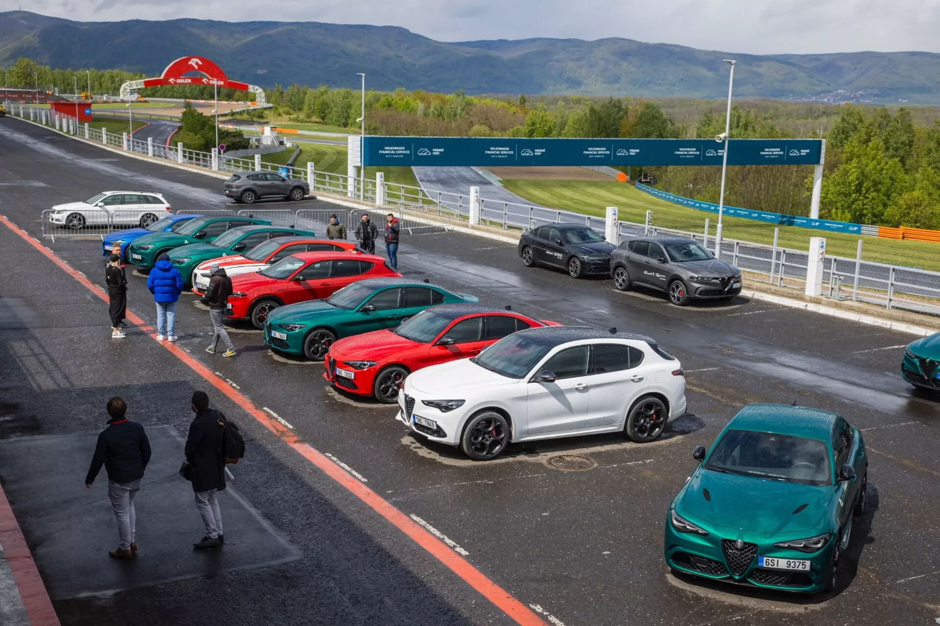 Alfa Romeo Giulia Quadrifoglio 2023 sur un circuit pittoresque, présentant un design aérodynamique élégant parmi une gamme de véhicules sportifs et de luxe sous un ciel partiellement nuageux