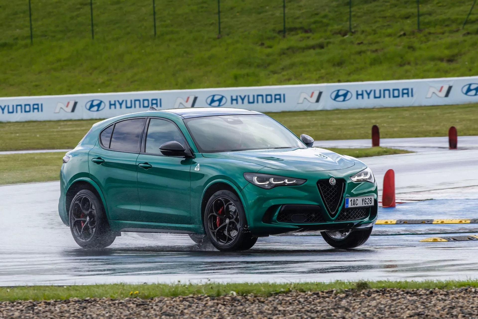 Vue dynamique de trois quarts avant du SUV vert orienté performance Alfa Romeo Giulia Quadrifoglio 2023 sur un circuit humide, montrant un style agressif, de grandes roues, et des fonctionnalités de sécurité avancées