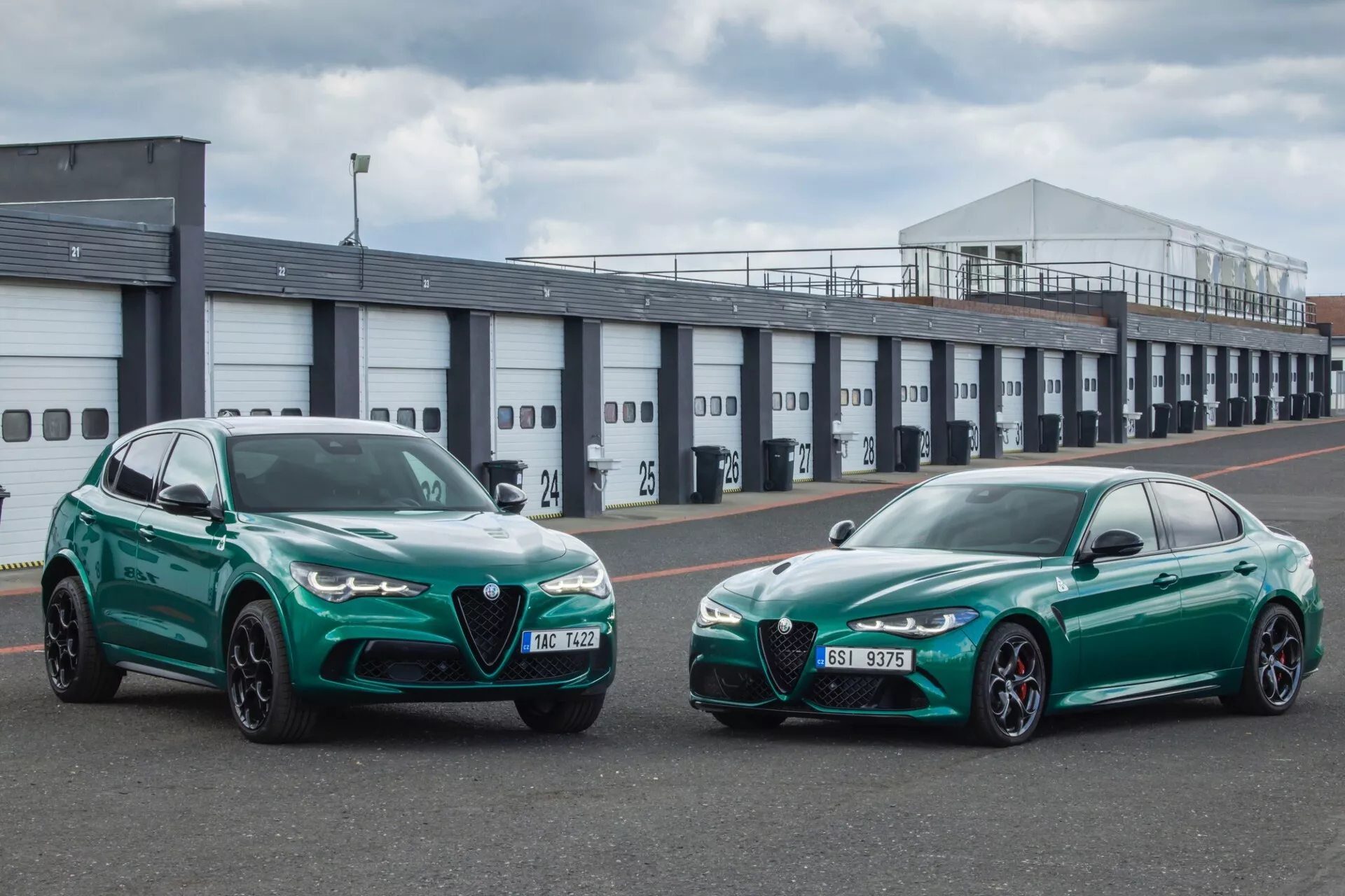 Alfa Romeo Giulia Quadrifoglio 2023 et SUV côte à côte en vert vibrant, montrant les profils avant et le design sportif contre un arrière-plan industriel avec des vibrations de piste de course, indiquant des caractéristiques de performance telles que les phares LED, les améliorations aérodynamiques et les freins haute performance.