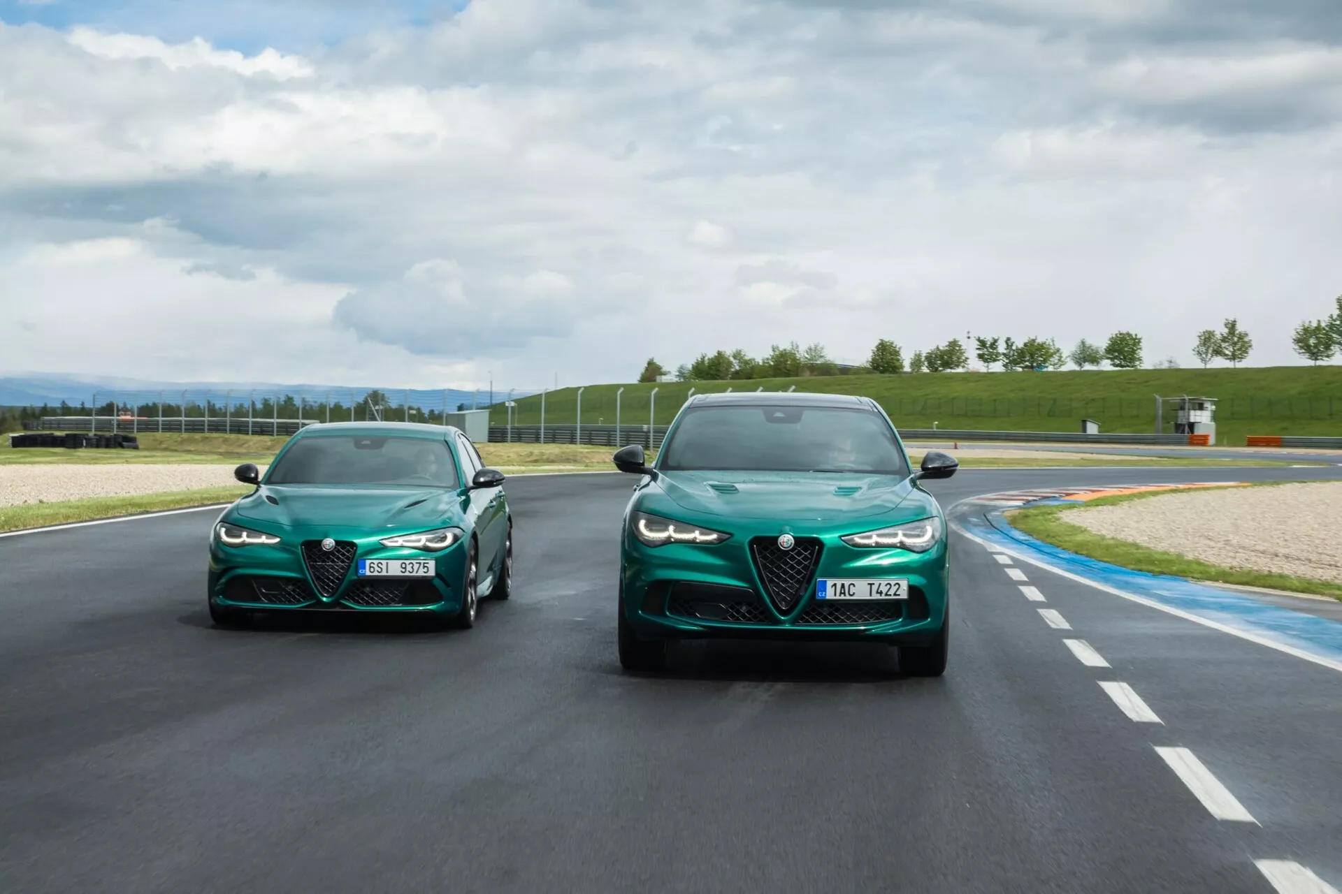 Voitures de sport Alfa Romeo Giulia Quadrifoglio 2023 roulant sur une piste sous la lumière naturelle du jour avec un ciel partiellement nuageux en arrière-plan, mettant en avant des lignes élégantes, un design aérodynamique et des caractéristiques de performance telles que des phares aiguisés et des prises d'air