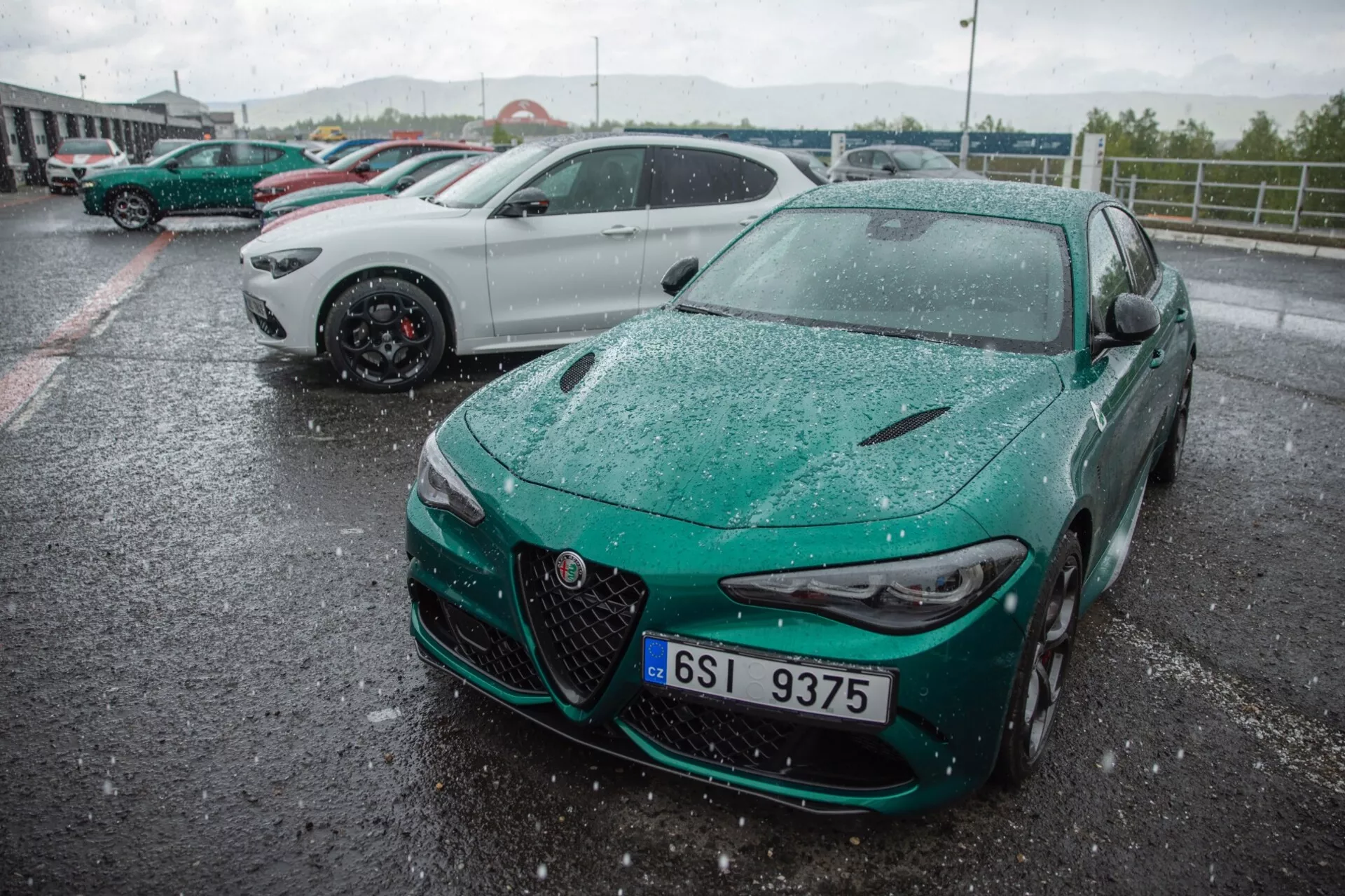 Alfa Romeo Giulia Quadrifoglio 2023 capturée sous un angle avant trois quarts mettant en évidence son design sportif, calandre proéminente avec badge central, phares LED élancés et pare-chocs avant aérodynamique dans un cadre extérieur mouillé par la pluie