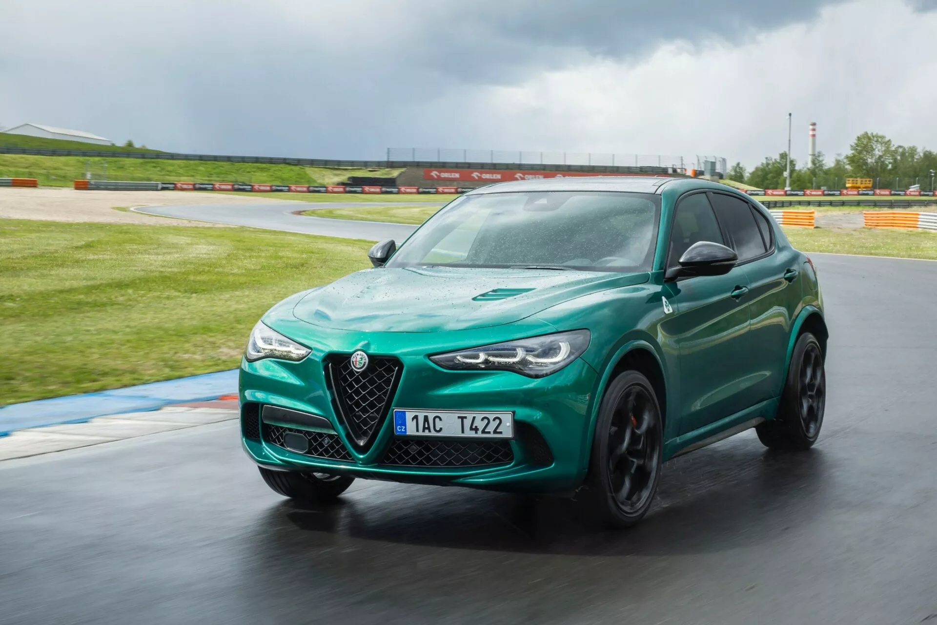 Alfa Romeo Giulia Quadrifoglio 2023 en vert métallique, négociant dynamiquement un virage sur un circuit, mise en valeur par sa façade avant agressive, ses phares LED élégants et sa posture sportive, soulignée par des caractéristiques technologiques telles que l'aérodynamique avancée et les freins haute performance.