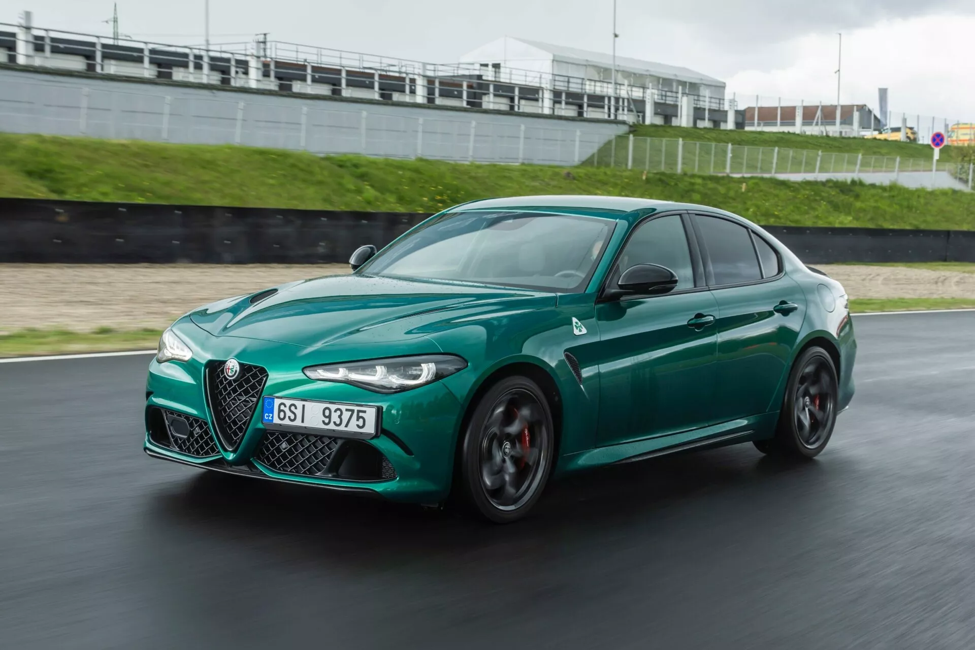 Alfa Romeo Giulia Quadrifoglio 2023 en mouvement sur circuit, vue avant dynamique trois quarts montrant un style agressif, une conception aérodynamique, la grille distinctive 'Trilobe', des phares LED élégants, de grandes prises d'air et des roues sportives de couleur graphite avec des étriers de frein rouges