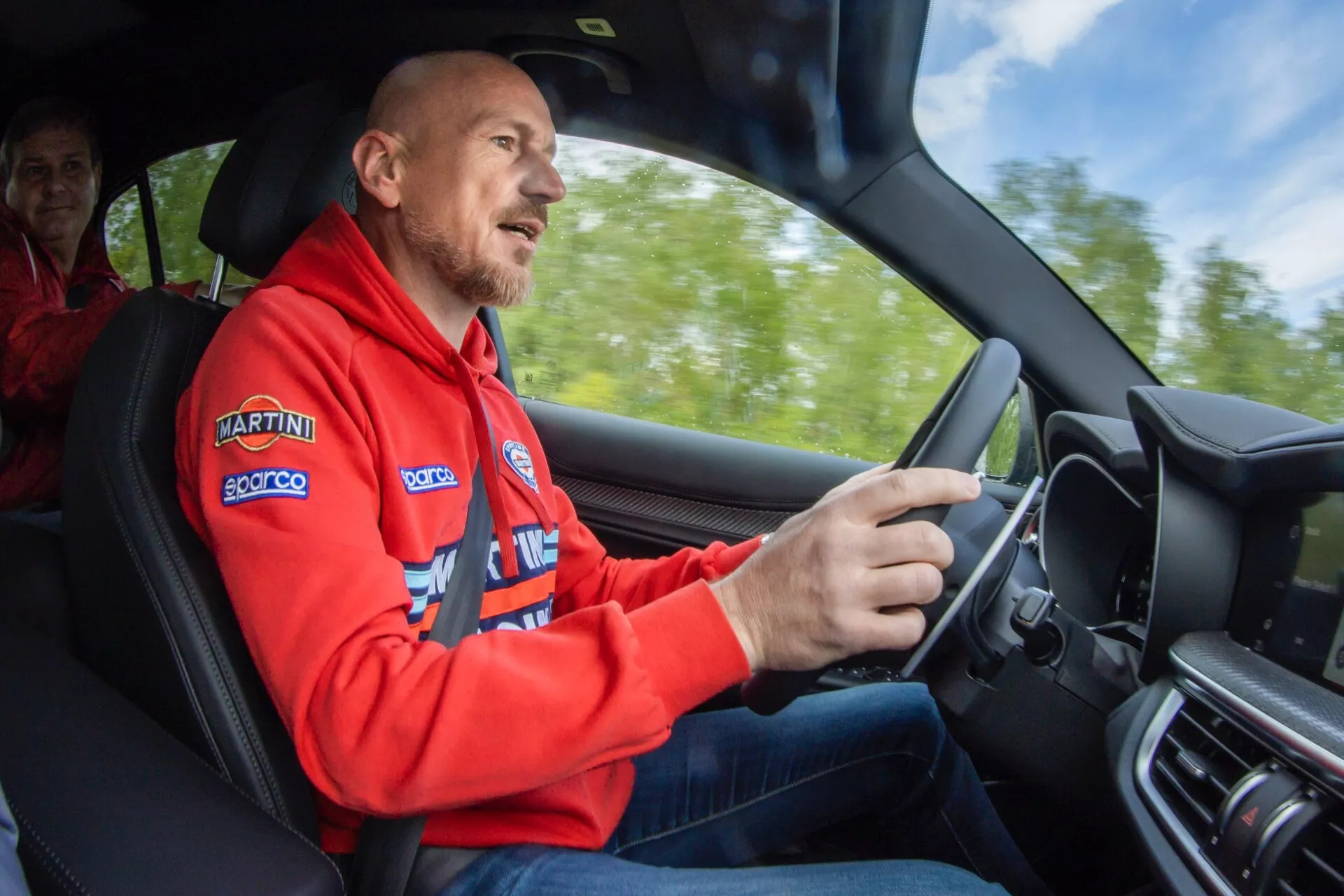 Vue intérieure d'une voiture sport-luxe du point de vue du conducteur en mouvement, montrant des caractéristiques comme un volant sportif, un rembourrage de porte sophistiqué, et un design de console centrale haut de gamme, indicatif d'un véhicule moderne équipé pour la performance et le confort.