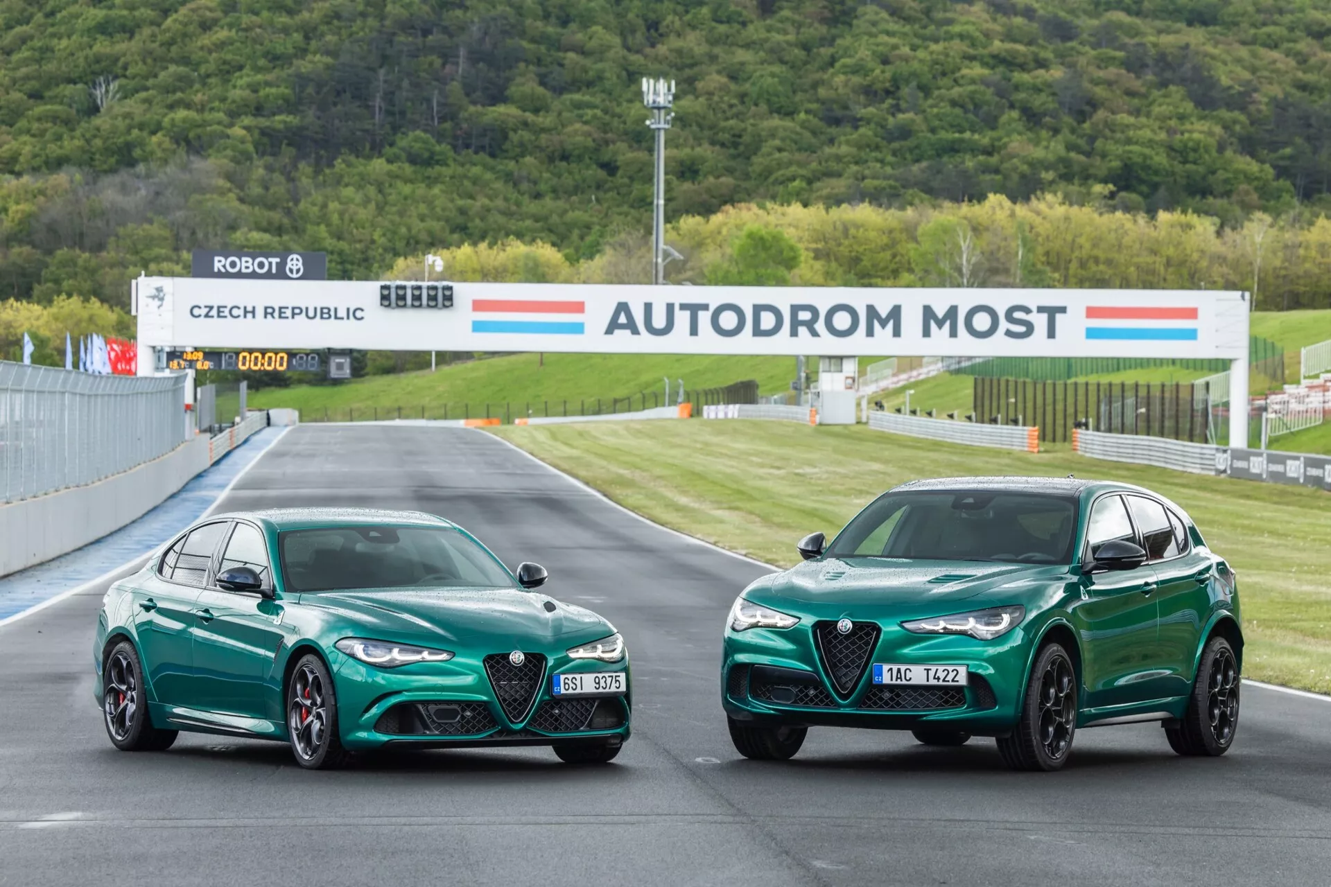 Alfa-Romeo Giulia Quadrifoglio et modèle SUV de 2023 garés sur un circuit, présentant les profils avant et latéral avec un accent sur les caractéristiques de performance telles que le design aérodynamique, les phares LED et la couleur verte distinctive sous l'éclairage professionnel de circuit