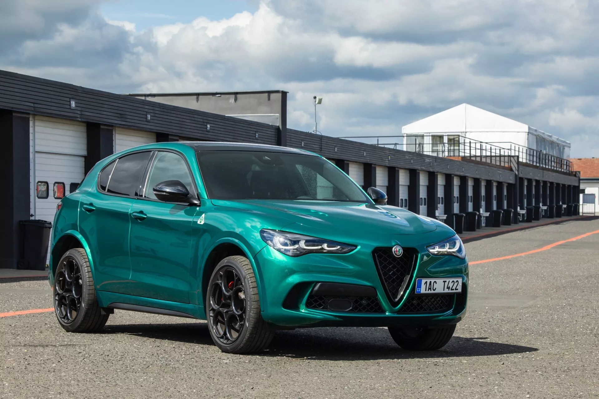 Alfa Romeo Giulia Quadrifoglio 2023 en vert métallique avec grille avant distincte en forme de bouclier et phares LED élégants, photographiée sous un angle avant de trois quarts soulignant les caractéristiques de design sportif et luxueux sur une piste de course.