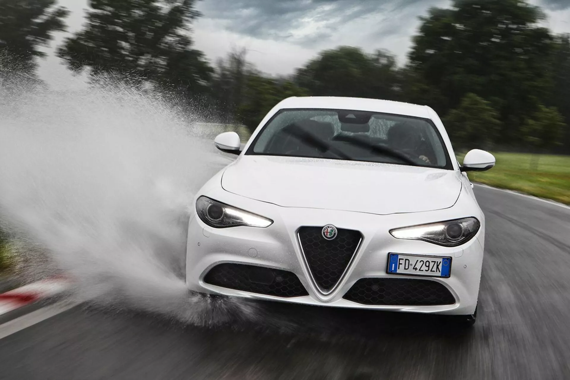 Alfa Romeo Giulia blanche de 2016 avançant à grande vitesse à travers l'eau, provoquant une éclaboussure, dans une vue de trois quarts avant mettant en évidence ses phares LED, sa calandre distinctive, ses rétroviseurs latéraux élégants et ses lignes aérodynamiques