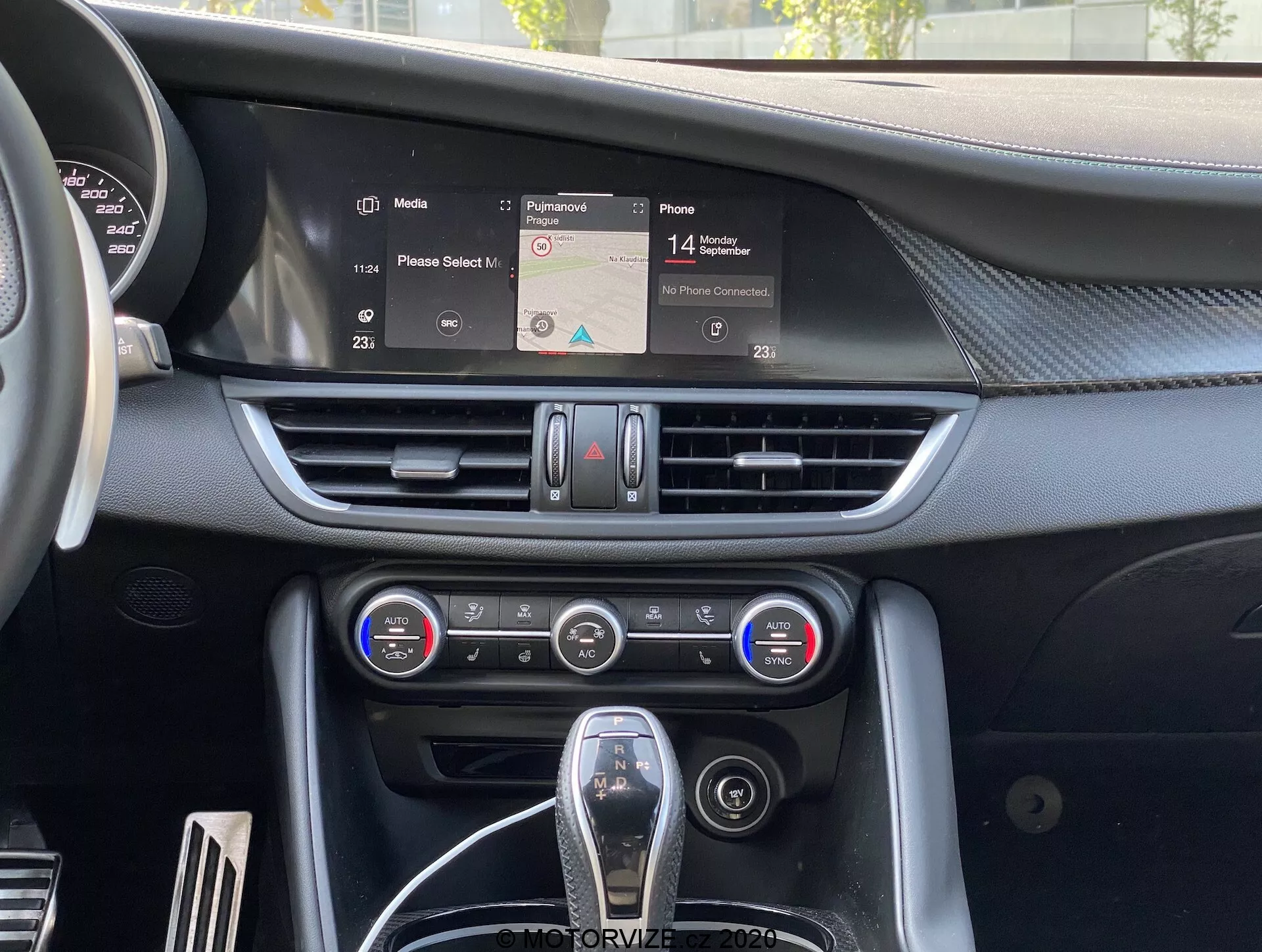 Vue intérieure de l'Alfa-Romeo Giulia 2016 se concentrant sur le tableau de bord central avec un écran d'infodivertissement affichant une carte de navigation, des bouches d'aération horizontales, un panneau de contrôle climatique bi-zone avec des cadrans et des boutons, et un sélecteur de vitesse partiellement visible avec garniture en cuir et accents chromés, représentant l'ergonomie et la technologie modernes de l'intérieur des voitures.