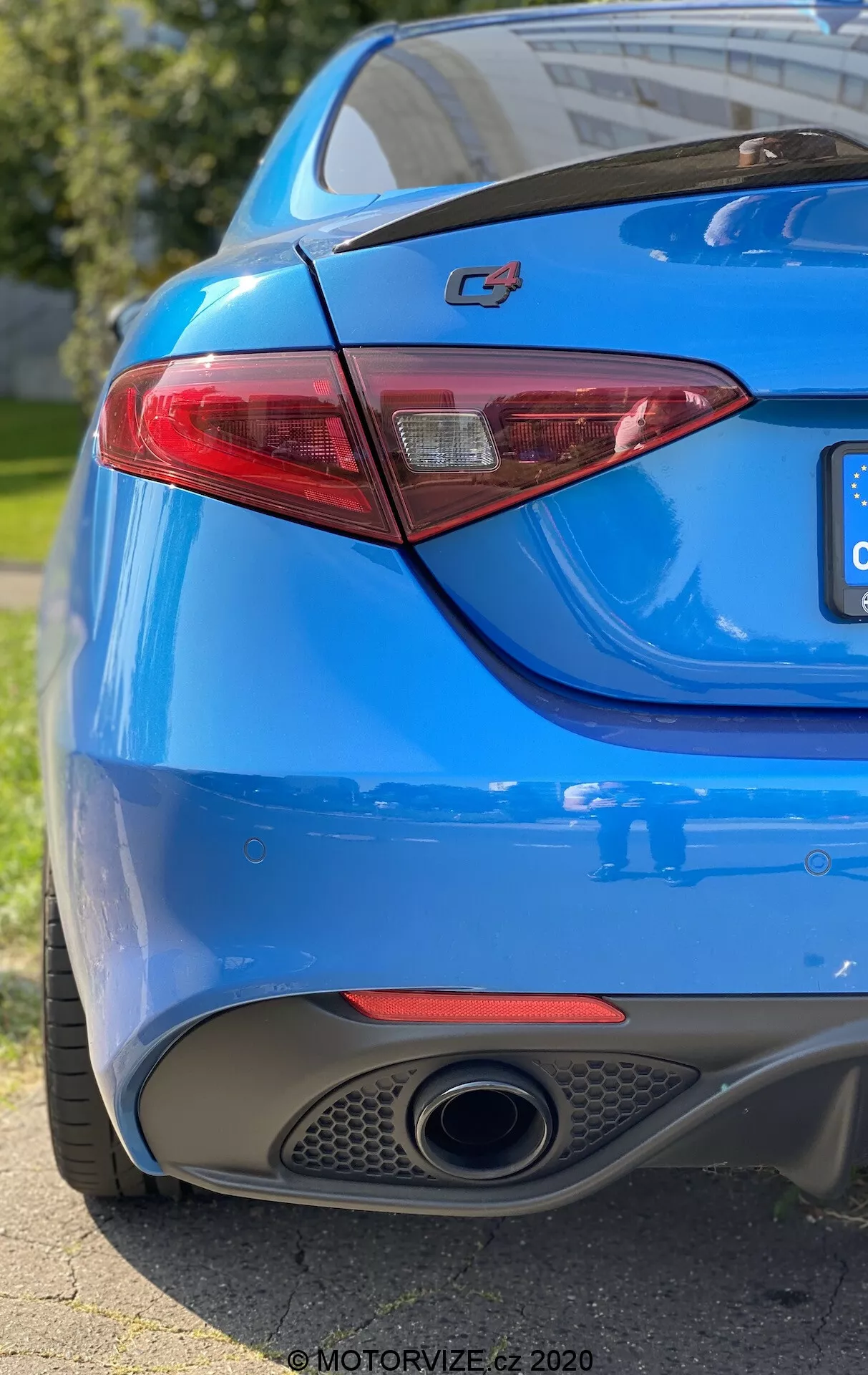 Gros plan de la section arrière d’une voiture bleue montrant le côté droit sous un angle de trois quarts bas. Le cadre capture le logo 'C4' proéminent sur le coffre, un feu arrière LED élégant, une peinture bleue vibrante, un seul tuyau d'échappement chromé et le diffuseur intégré dans le pare-chocs arrière. La faible profondeur de champ met en évidence le logo et le feu arrière, tandis que la lumière naturelle du soleil se reflète sur les courbes lisses et sportives de la carrosserie.