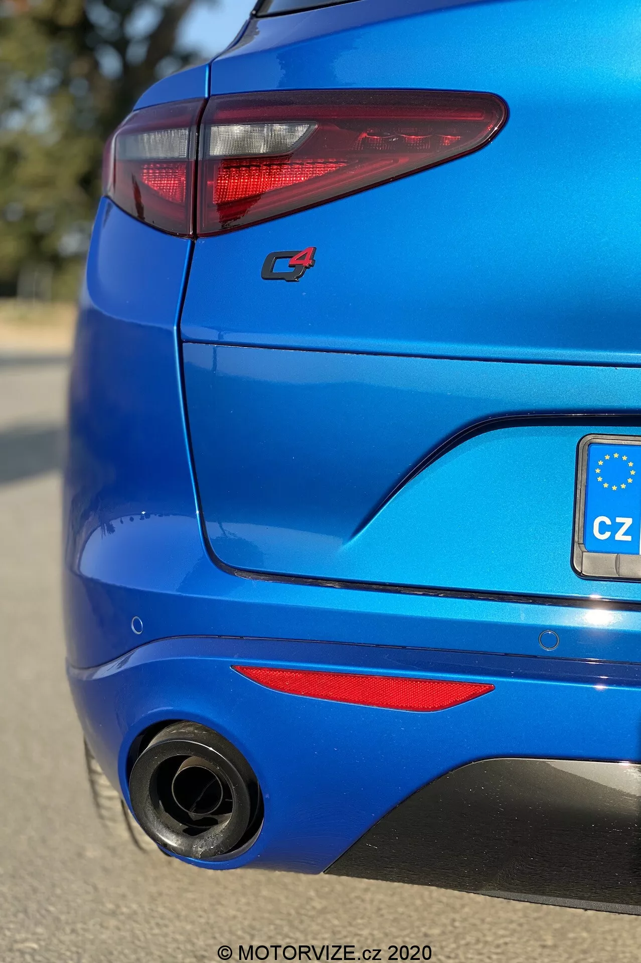 Gros plan de la section arrière d'une Alfa Romeo Stelvio bleu vif de 2017, pris en contre-plongée vers la droite et se concentrant sur l'angle arrière. Comprend des feux arrière à LED en forme de C élégants, un badge sportif rouge 'S', un pare-chocs arrière avec élément diffuseur et insert noir, un grand embout d'échappement circulaire à gauche, une peinture bleue métallisée, des réflecteurs rouges, et un petit spoiler de toit, mettant en valeur le design moderne et l'esthétique sportive du véhicule.