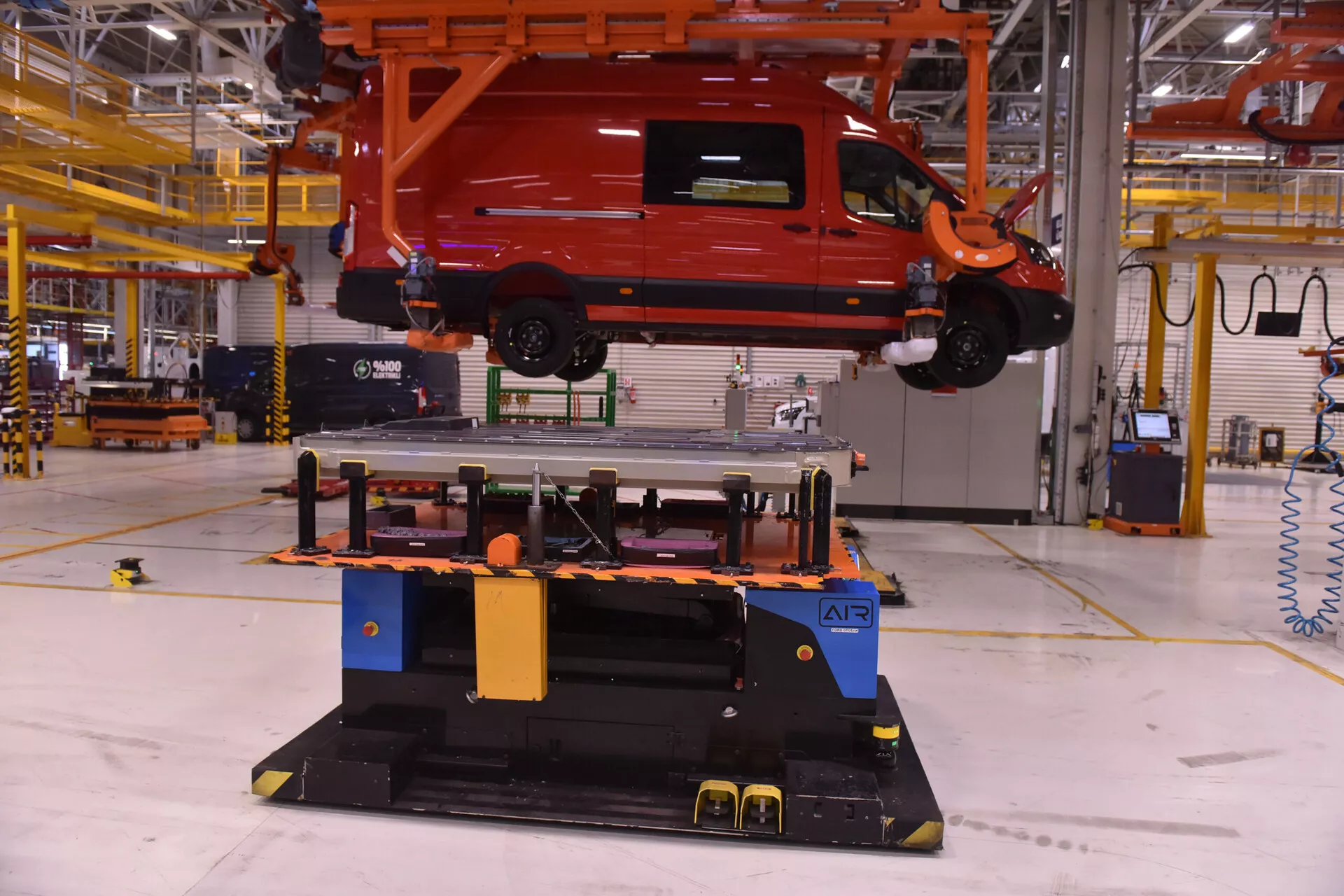 Alfa Romeo Stelvio de 2017 en rouge vif, suspendu par une grue dans un cadre industriel d'usine, montrant le processus d'assemblage du véhicule avec une vue de côté et arrière