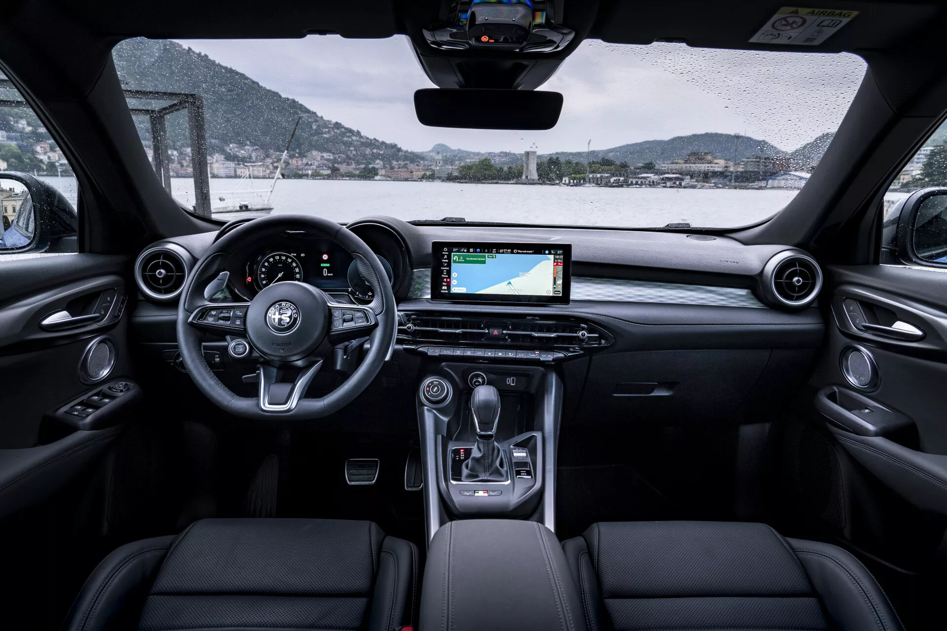 Vue intérieure d'une Alfa Romeo Tonale 2022 montrant le tableau de bord, le volant, la zone de la cabine avant, l'écran numérique avec navigation, la console centrale et les sièges avant tapissés depuis une perspective des sièges arrière