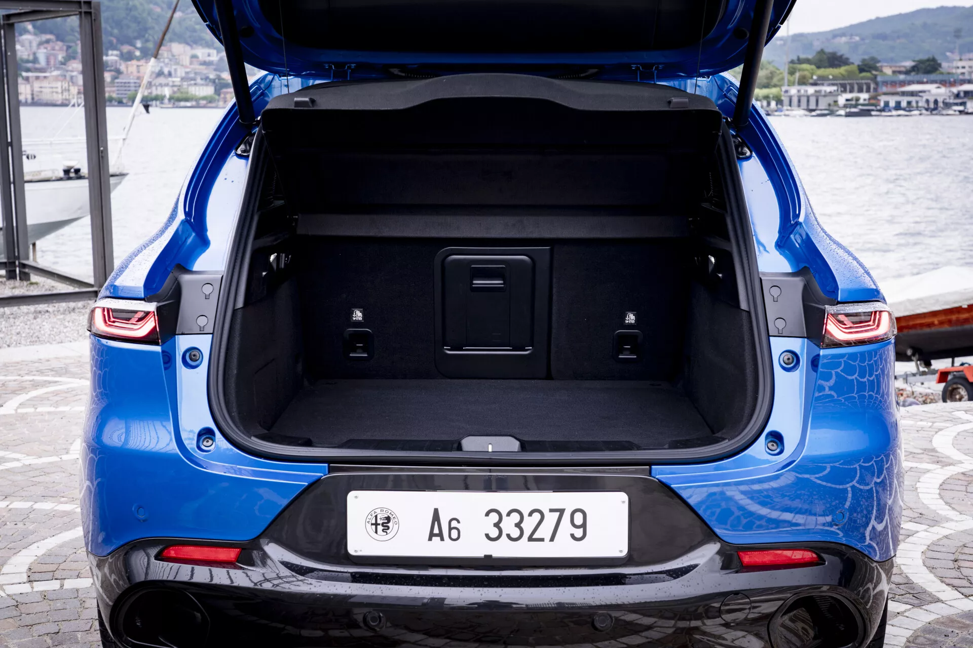Vue arrière d'une Alfa-Romeo Tonale bleue 2022 avec le coffre ouvert, montrant une peinture métallique, la plaque d'immatriculation clairement visible, des feux arrière LED, un emblème de la marque sur le hayon et un espace de chargement spacieux et propre.