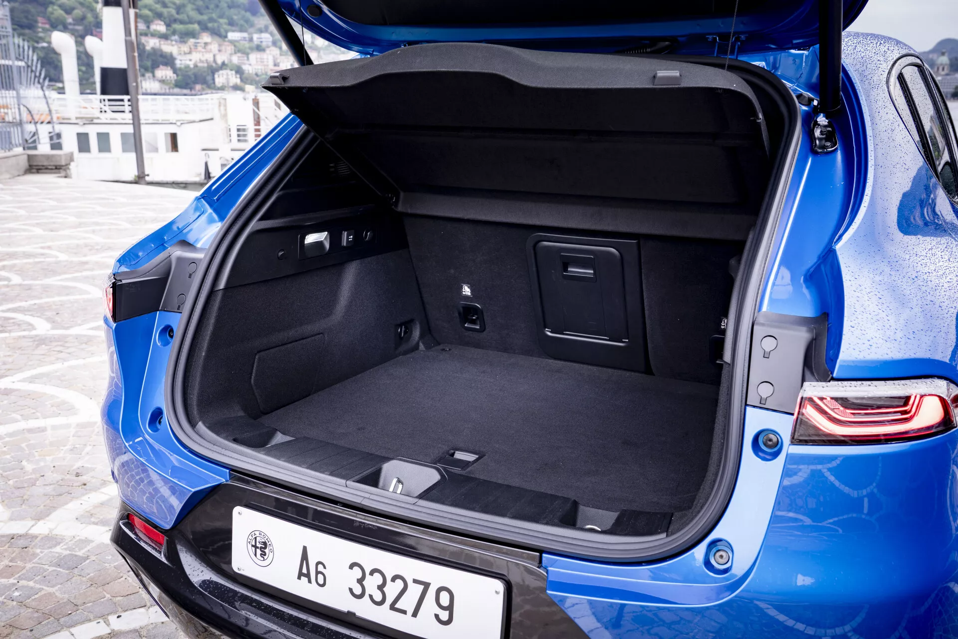 Alfa Romeo Tonale bleue 2022, vue arrière en trois quartiers montrant le coffre hatchback ouvert et le côté gauche de la carrosserie, mettant en lumière l'espace de chargement et les détails de conception