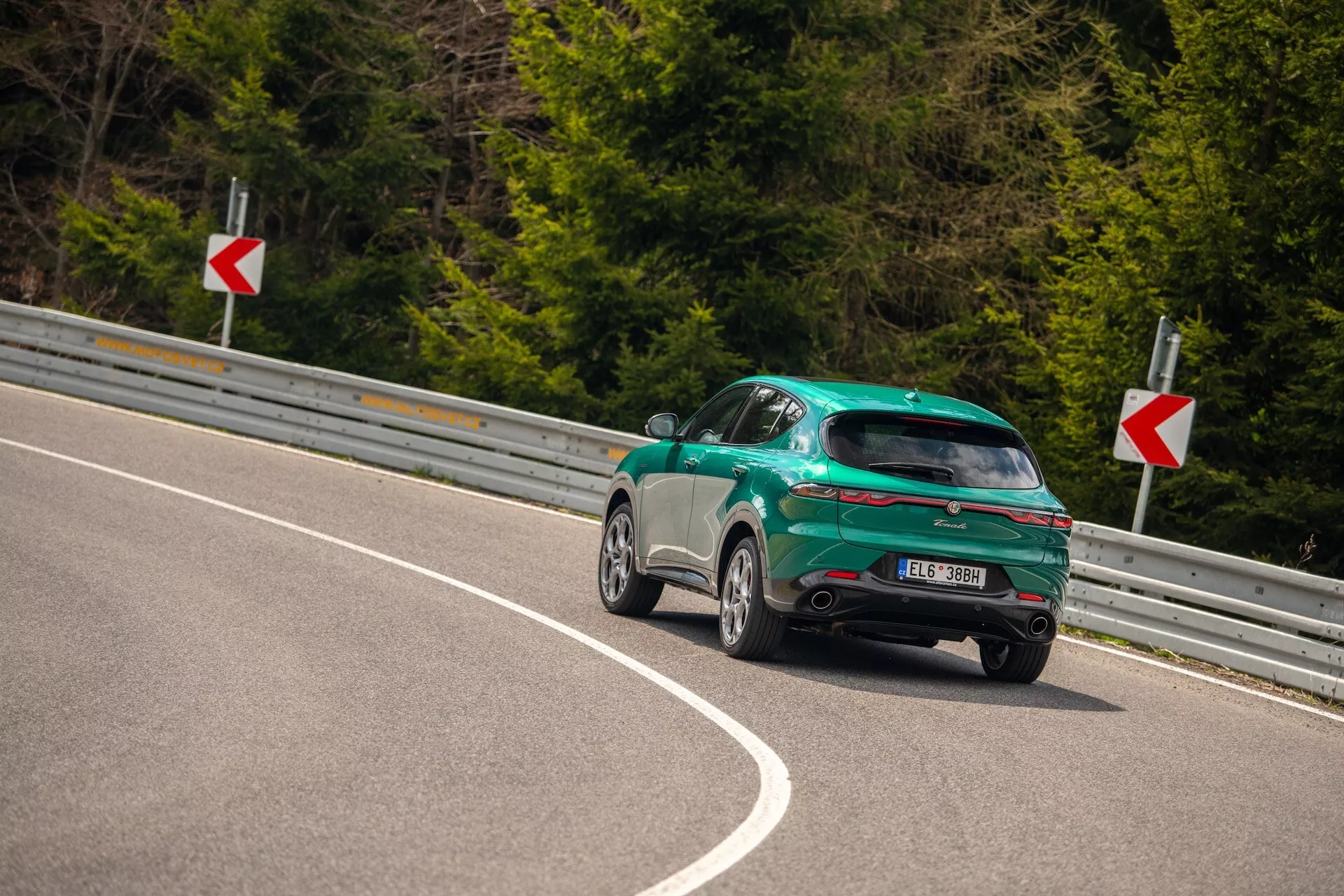 Alfa Romeo Tonale 2022 capturée depuis un angle arrière de trois quarts sur une route courbe, mettant en valeur son design sportif avec hayon, finition brillante et caractéristiques aérodynamiques dont un spoiler arrière, des jantes alliage et des feux arrière LED.