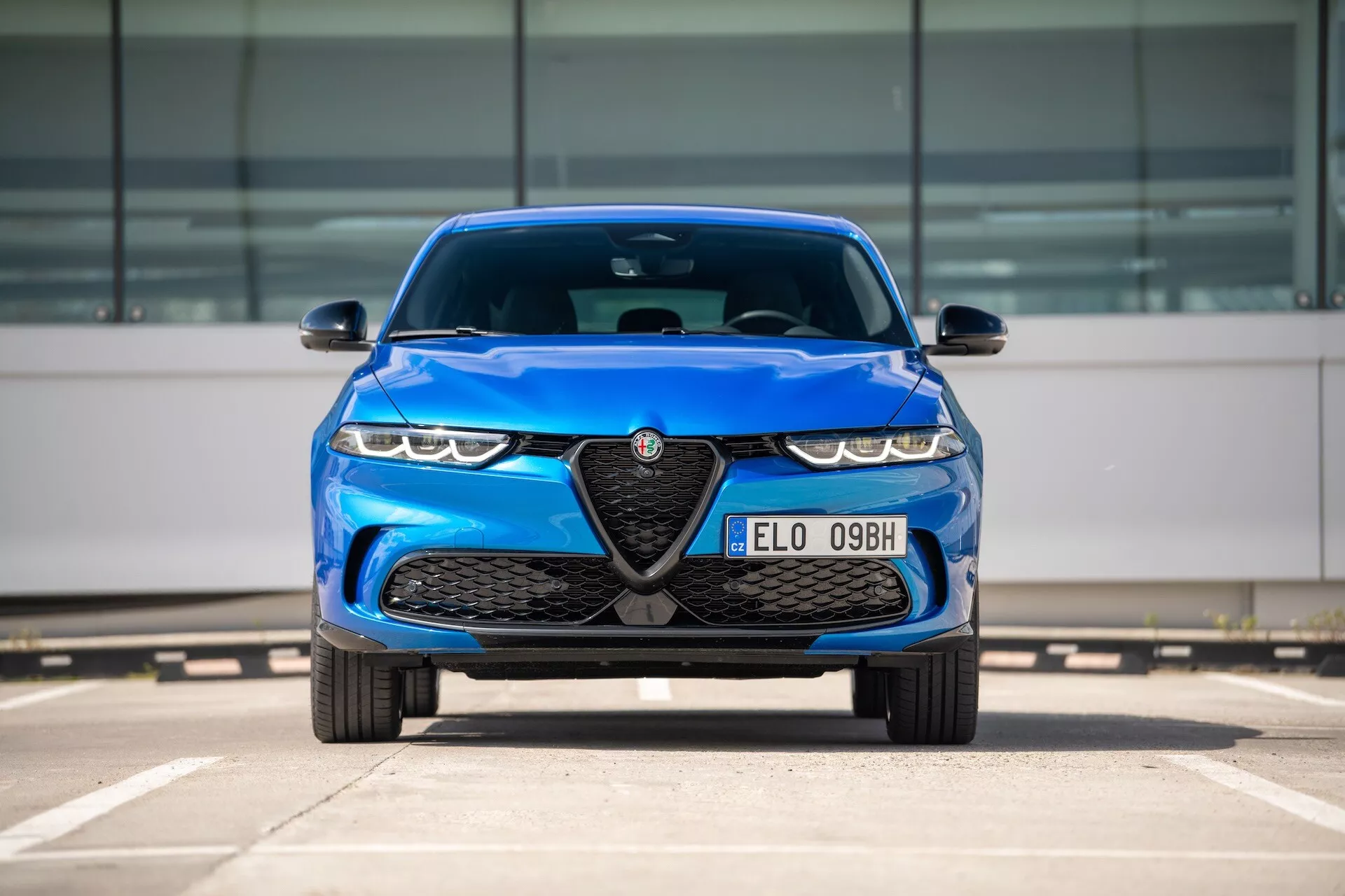 Alfa Romeo Tonale 2022 en bleu, vue de face sur un parking mettant en avant la calandre avec emblème, phares LED et caractéristiques de design aérodynamique
