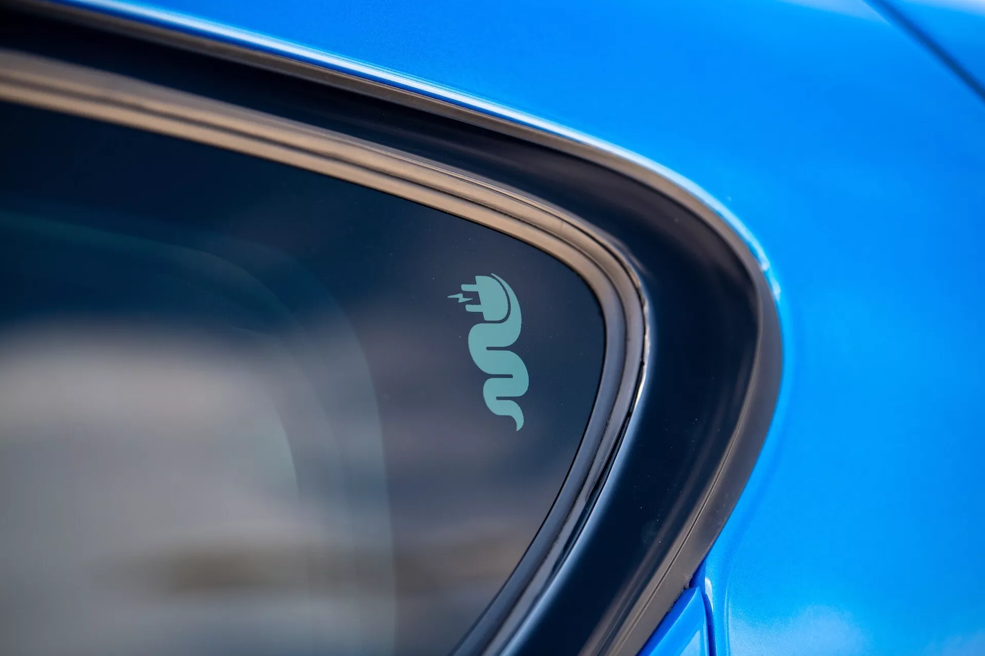 Gros plan détaillé sur le badge technologique de l'Alfa Romeo Tonale 2022 indiquant une capacité électrique ou hybride près de la fenêtre de la voiture, mis en évidence par une peinture bleue réfléchissante et un design élégant à la lumière naturelle du jour