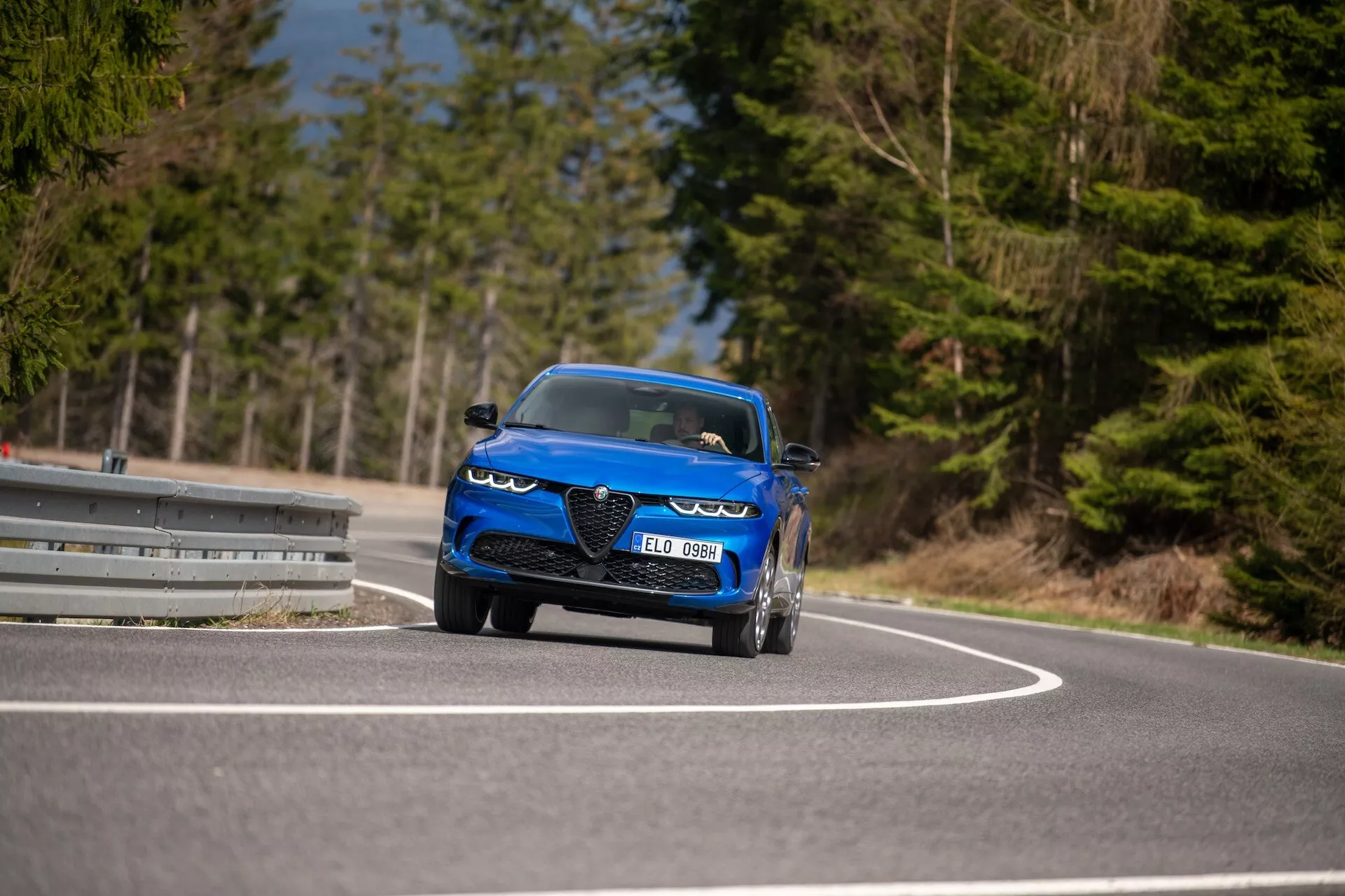 Alfa-Romeo Tonale 2022 en mouvement sur une route sinueuse, exhibant son design dynamique, phares LED, entrées d'air, style convertible sportif et caractéristiques de luxe depuis une perspective frontale de trois quarts en bas angle