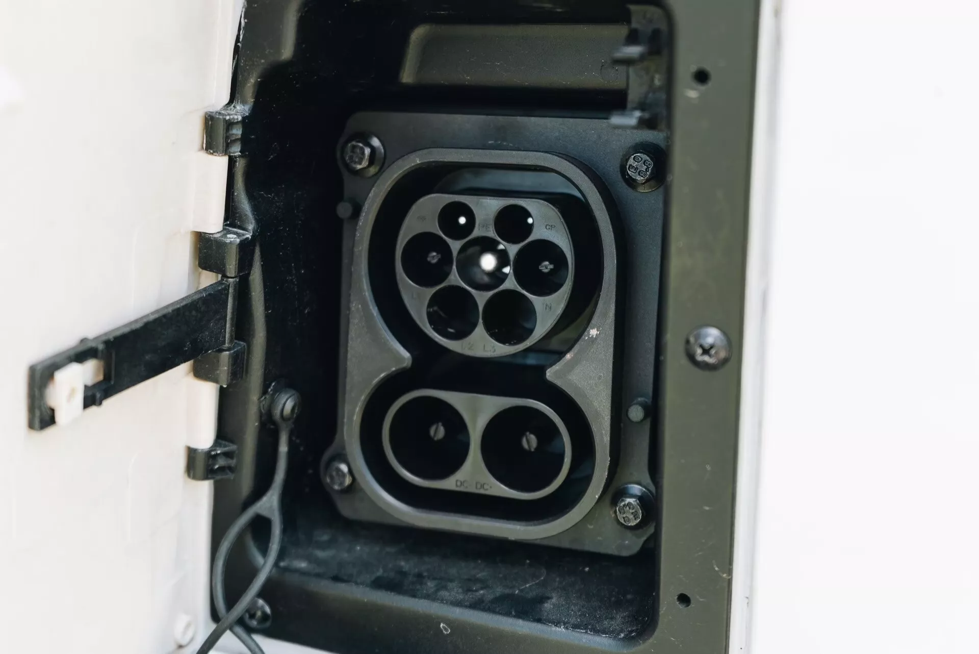 Vue de près d'une prise de charge pour véhicule électrique (VE) montrant deux designs de connecteur dans la même unité: un connecteur de type 2 avec une disposition à sept broches et une prise CHAdeMO avec quatre grandes broches et une broche de communication plus petite, indiquant une compatibilité avec plusieurs normes de charge VE. Le couvercle articulé est ouvert et un câble flexible est attaché, soulignant l'accent mis sur l'infrastructure VE, la technologie de charge et le transport durable.