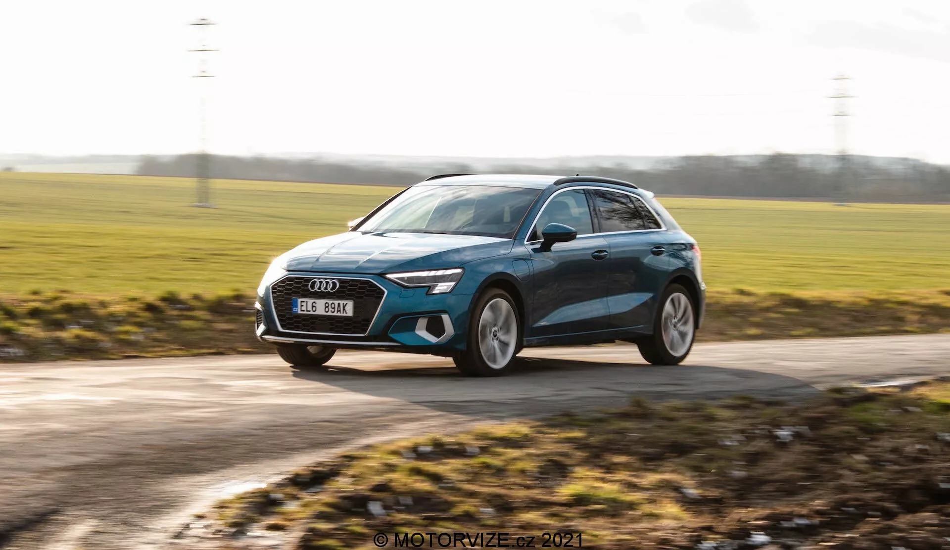 Cliché dynamique d'une berline compacte moderne, probablement l'Audi A3 Sportback 2020, capté en mouvement. L'image est prise sous un angle légèrement bas, mettant en valeur la hauteur de la voiture et créant une sensation dynamique. Elle montre une vue de trois quarts avant avec le véhicule se déplaçant de droite à gauche. Les éléments de design notables comprennent des phares LED élégants, une grande calandre avant, de grandes roues en alliage, des rétroviseurs latéraux profilés avec indicateurs de direction intégrés potentiels et une finition de peinture métallisée avec des lignes de contour. L'arrière-plan est flou, ce qui améliore la sensation de vitesse, tandis que la voiture elle-même reste nette, soulignant son design contemporain et son esthétique premium.