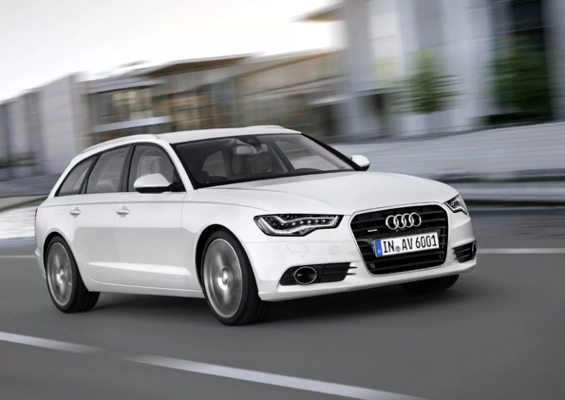 Audi A6 Avant blanche de 2011 en mouvement, capturée sous un angle bas de trois quarts avant mettant en évidence la calandre, les feux de jour à LED, les jantes en alliage et le design dynamique