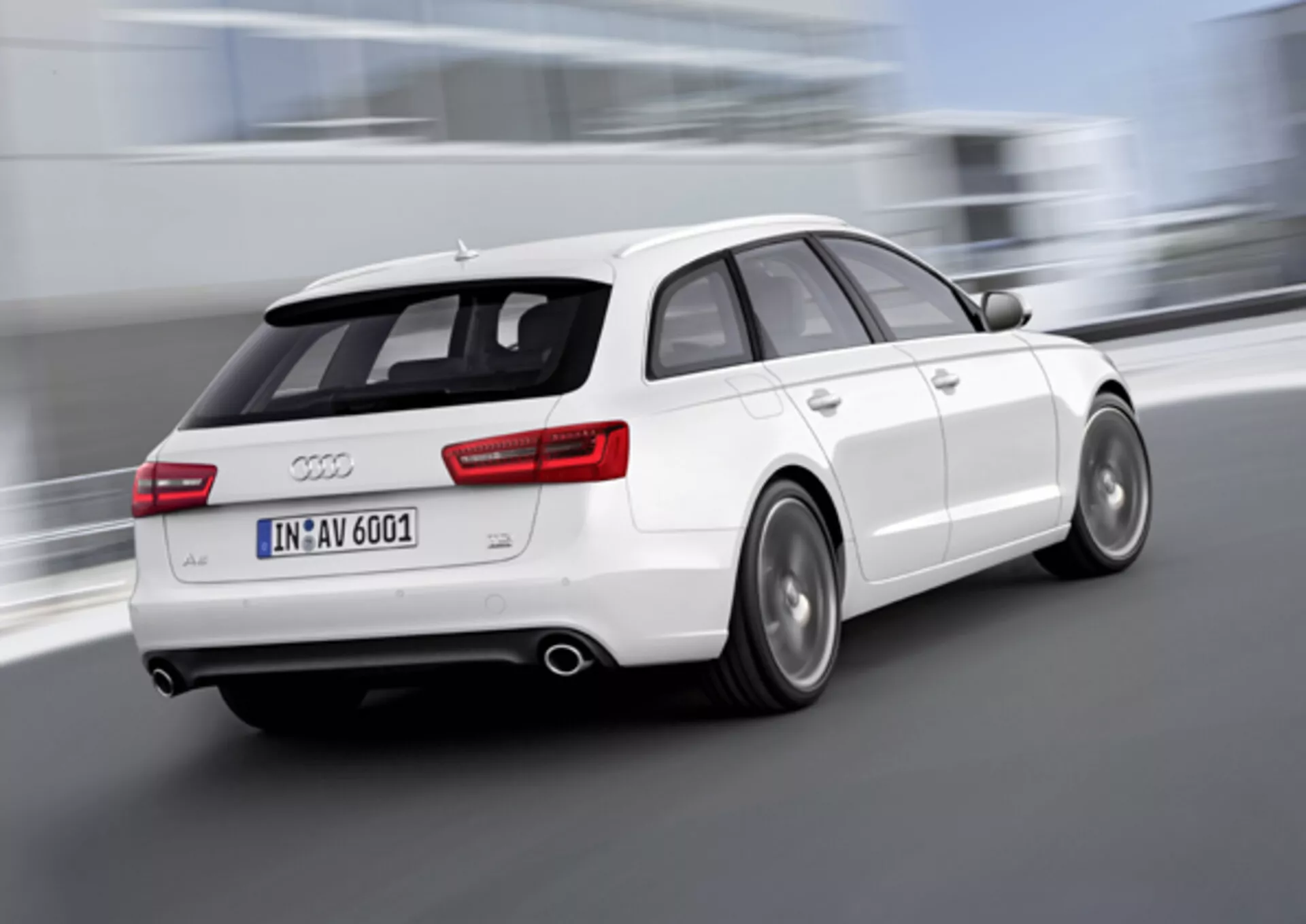 Vue arrière dynamique en trois quarts d'une Audi A6 Avant blanche de 2011 en mouvement, avec des roues floues indiquant la vitesse, un double échappement, des jantes en alliage avec freins à disque visibles, et un aileron monté sur le toit pour améliorer l'aérodynamique, prise en extérieur.