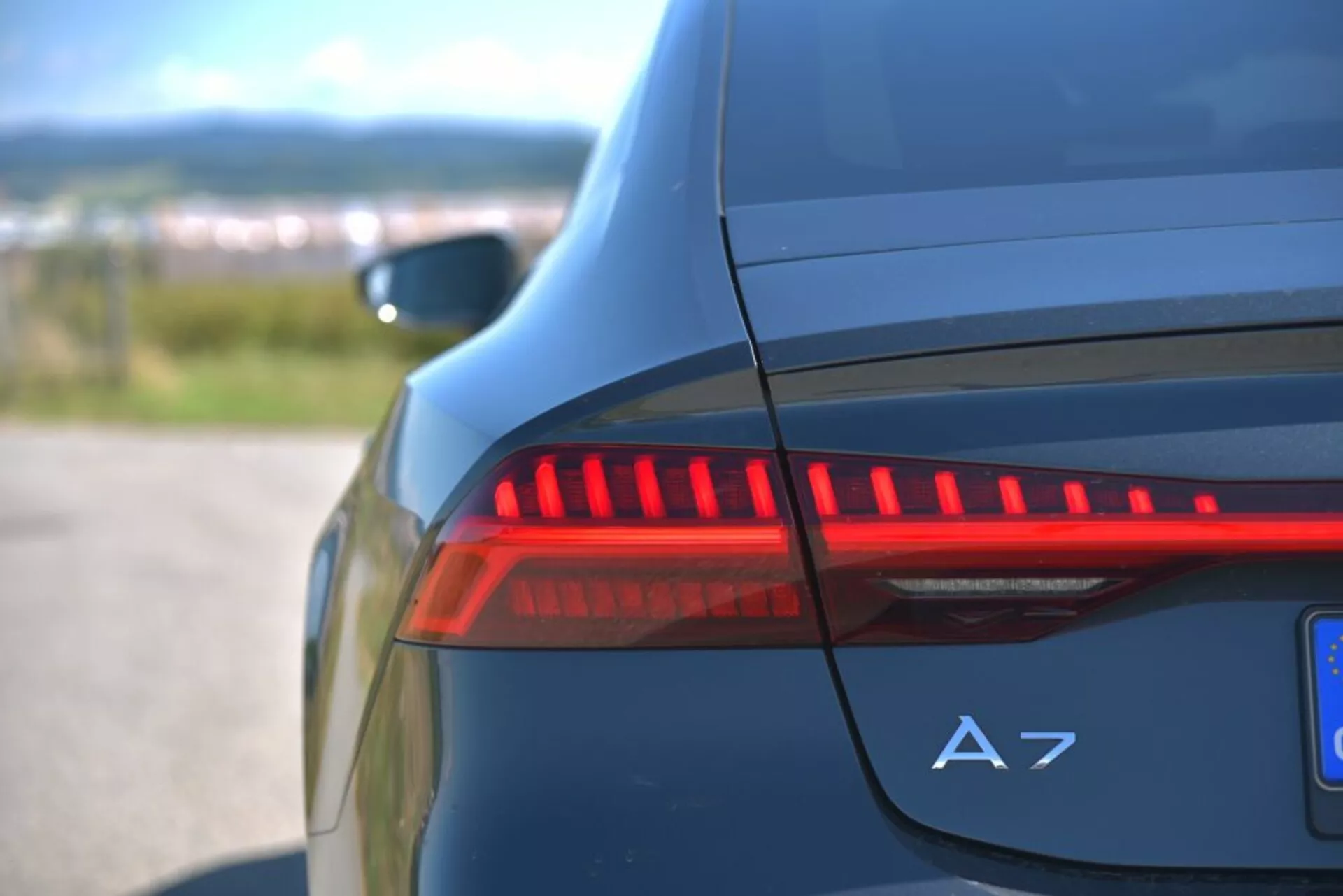 Vue rapprochée du feu arrière LED illuminé et du badge A7 sur le côté arrière d'une Audi A7 Sportback bleu foncé, mettant en évidence les caractéristiques du design automobile moderne et les détails de luxe