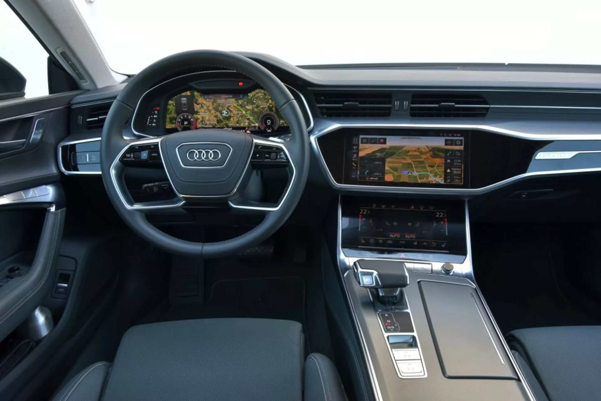 Vue intérieure de l'Audi A7 Sportback 2018 se concentrant sur le tableau de bord du conducteur et la zone de la console centrale, mettant en vedette un volant multifonctions à trois branches avec le logo Audi, un cluster d'instruments numérique Virtual Cockpit affichant la navigation, un système d'infodivertissement à double écran avec des réglages de contrôle climatique, un sélecteur de vitesse ergonomique et des matériaux haut de gamme comme le métal brossé et le cuir.