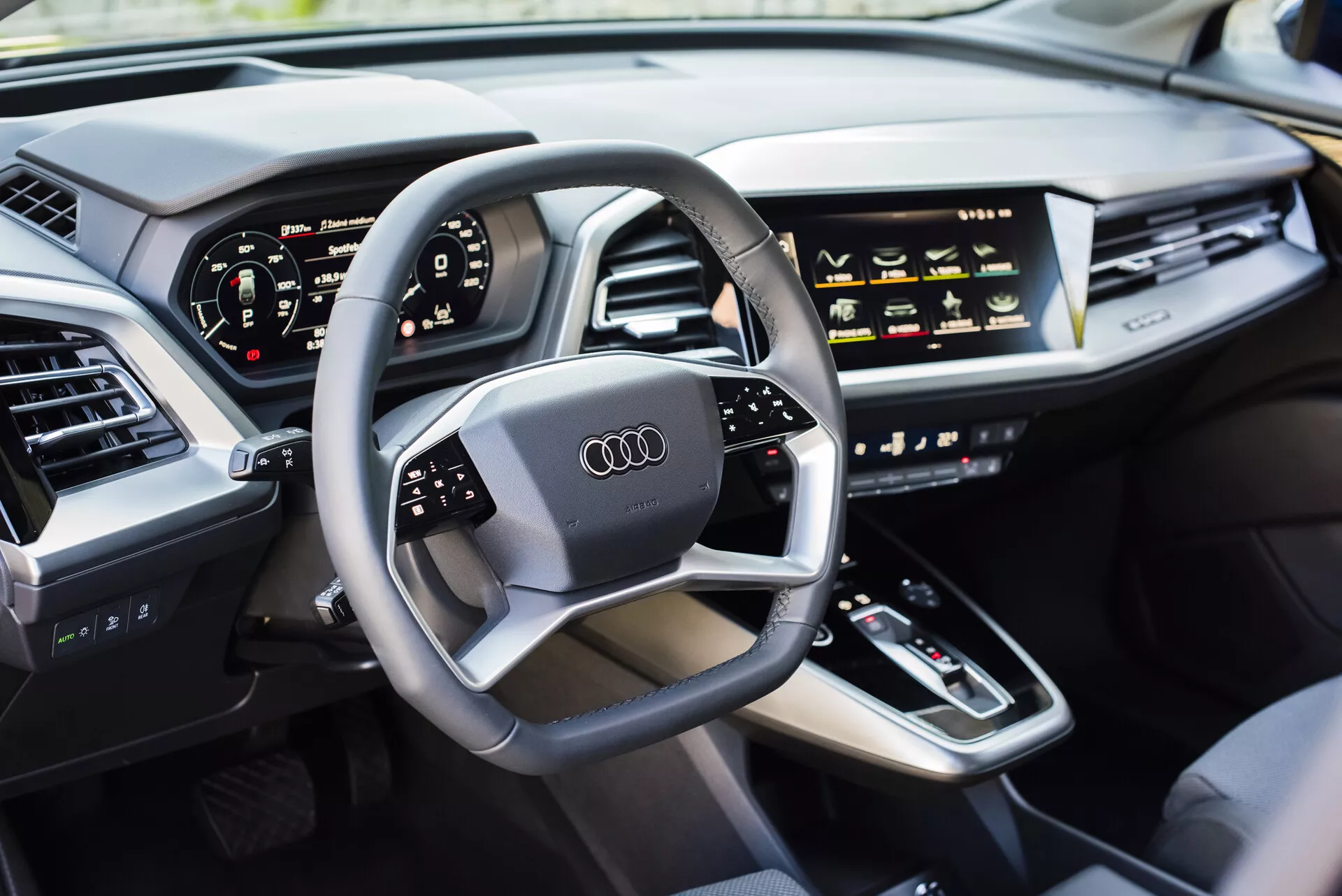Vue intérieure d'une Audi Q4 e-tron 2021 côté conducteur, présentant un volant multifonctionnel avec logo Audi, un tableau de bord numérique, une console centrale avec levier de vitesse, des commandes HVAC sensibles au toucher, un affichage d'infodivertissement, un tableau de bord élégant avec des bouches d'air intégrées, et une porte capitonnée en cuir de luxe, mettant en évidence la technologie automobile moderne et les caractéristiques des véhicules de luxe.