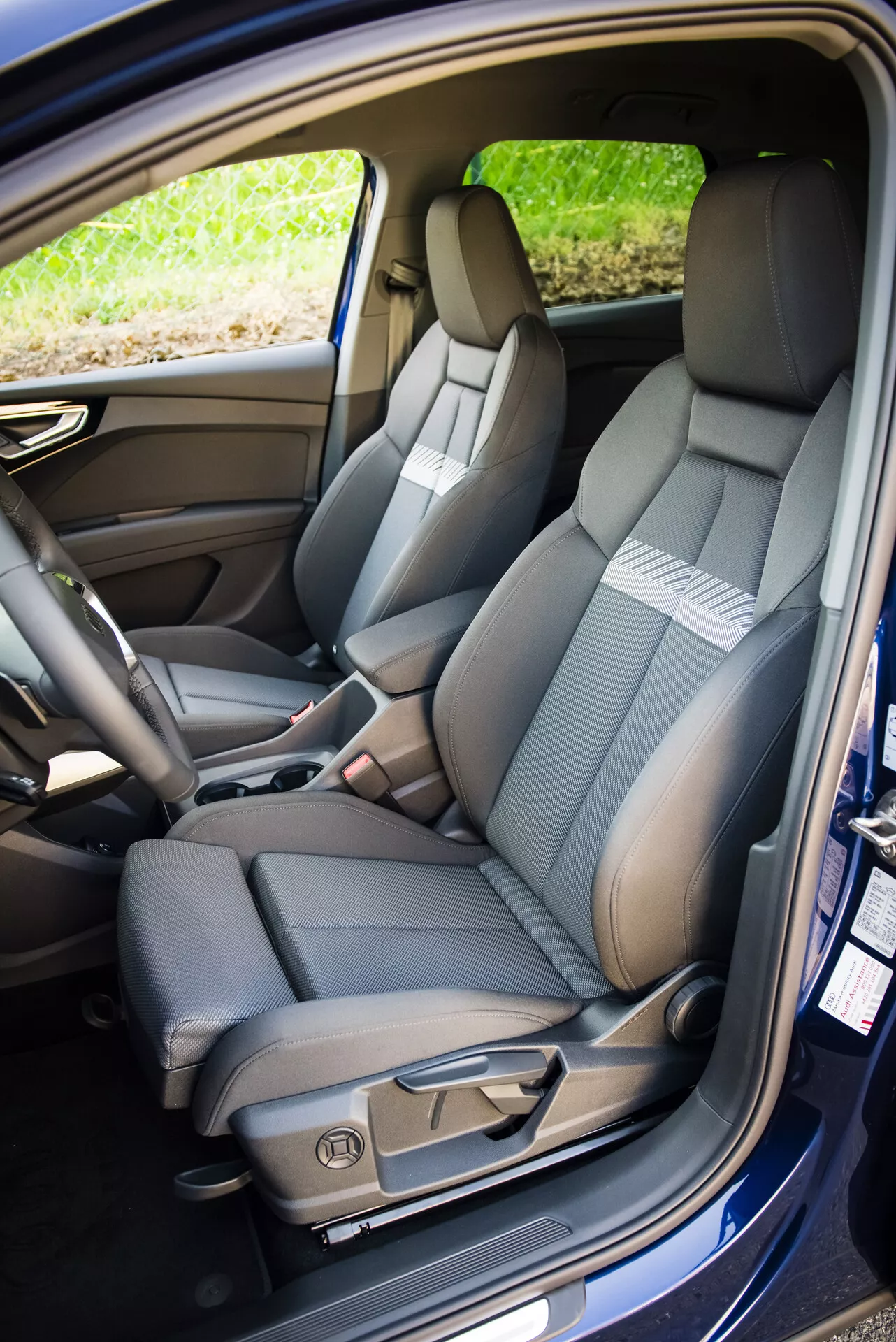 Intérieur de l'Audi Q4 e-tron 2021 présentant le siège avant côté passager avec sellerie bicolore, coutures détaillées, commandes de réglage électrique, et ceinture de sécurité, ainsi qu'un aperçu du siège arrière avec fonction de rabattement fractionné et des caractéristiques technologiques de l'habitacle.