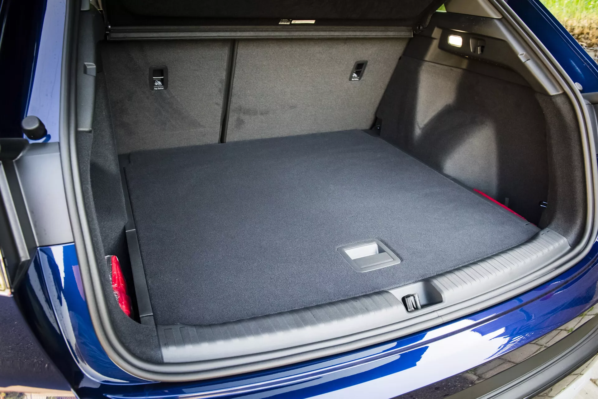 Vue de l'espace de coffre spacieux et moquetté de l'Audi Q4 e-tron 2021 avec le couvercle du coffre ouvert, montrant des solutions de rangement intelligentes et un aperçu de son extérieur bleu métallique avec capteur de stationnement visible