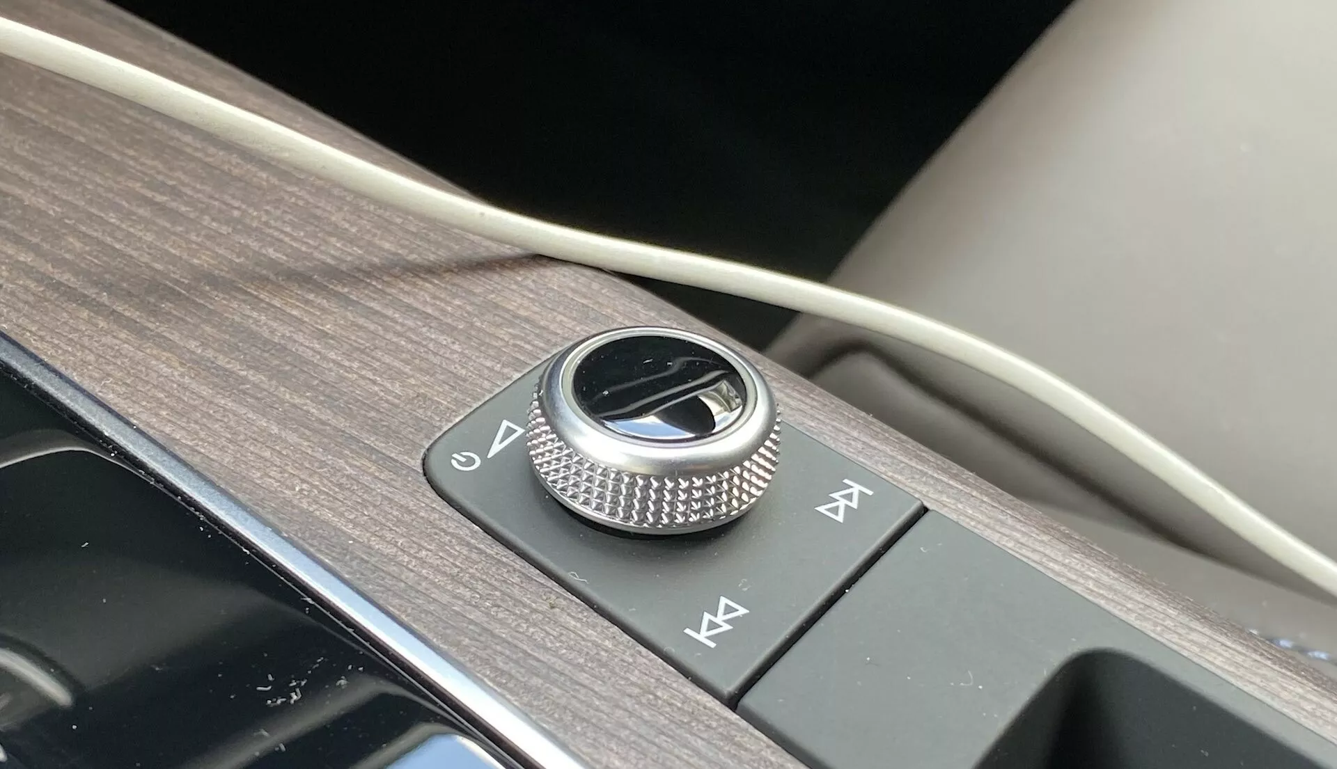 Gros plan sur la console centrale de l'Audi Q5 2020 Sportback, mettant en évidence un bouton rotatif métallique de commande d'infodivertissement entouré de garnitures en métal brossé sur un panneau noir brillant. À côté, deux boutons d'accès rapide, l'ensemble sur une surface texturée en grain de bois avec une touche de matériau doux, illustrant le design intérieur d'une voiture de luxe et les fonctionnalités avancées du système d'infodivertissement.